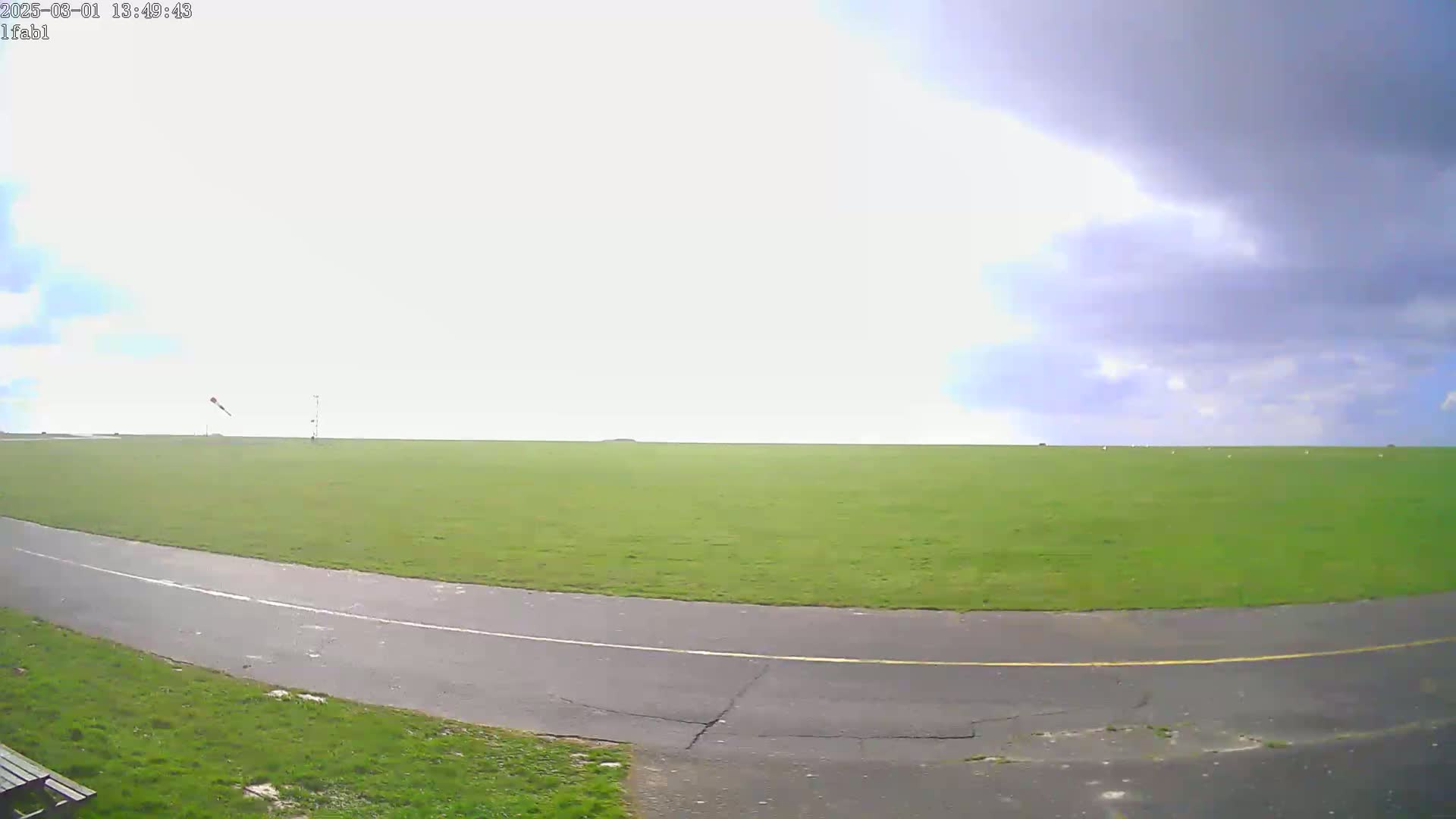 A paved roadway curves through a large, grassy field under a partly cloudy sky.