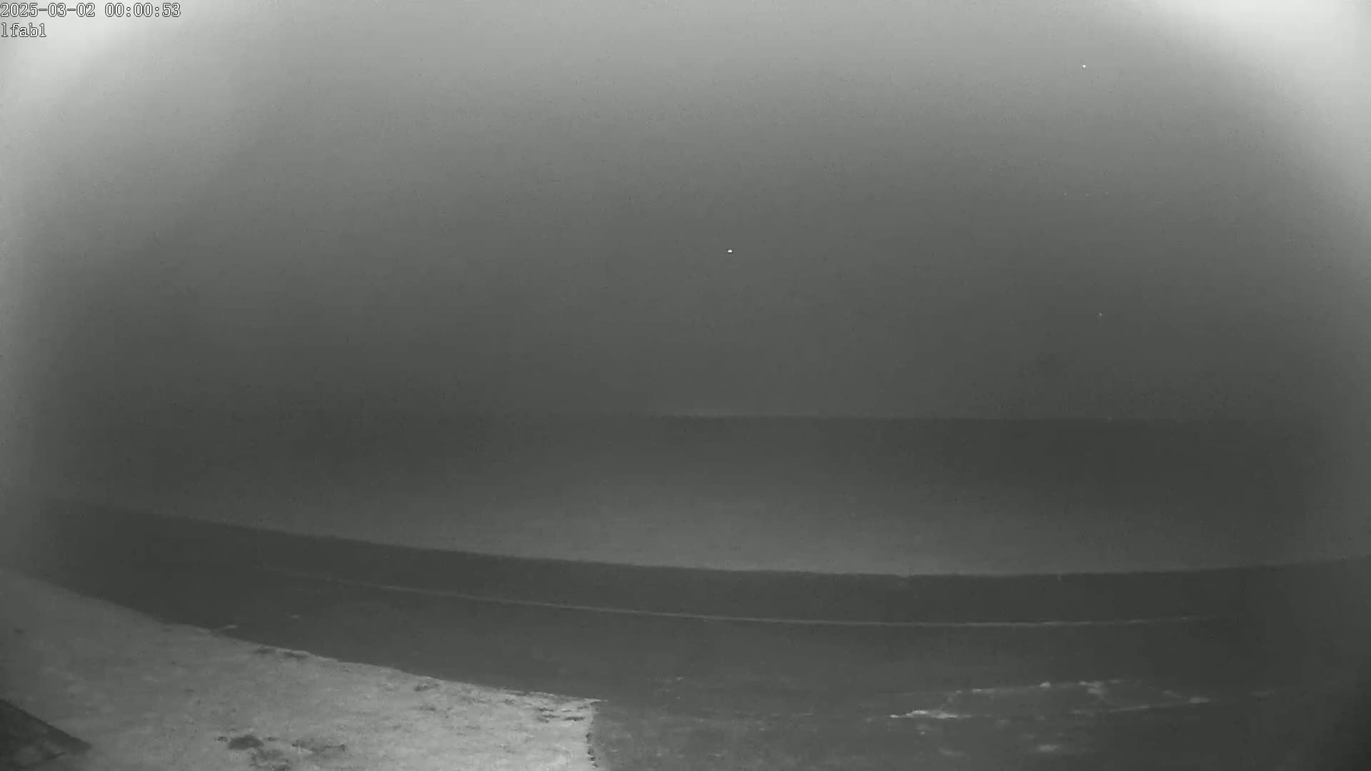 A low-light, grainy image shows a dark, flat expanse of water under a foggy sky.