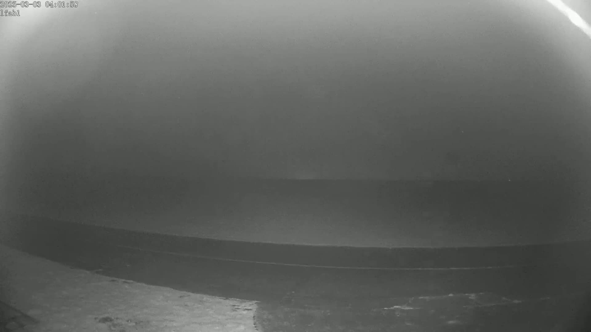 A low-light, grainy image shows a dark body of water under a foggy sky.