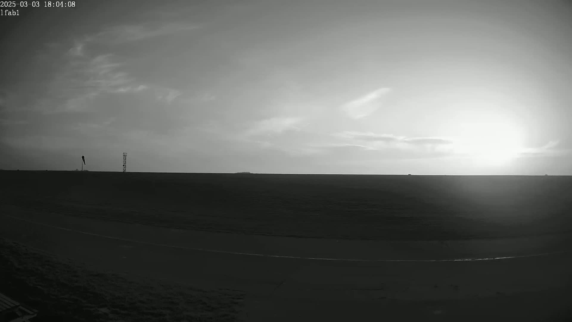 A flat, dark landscape stretches to a bright horizon under a mostly cloudy, light sky.