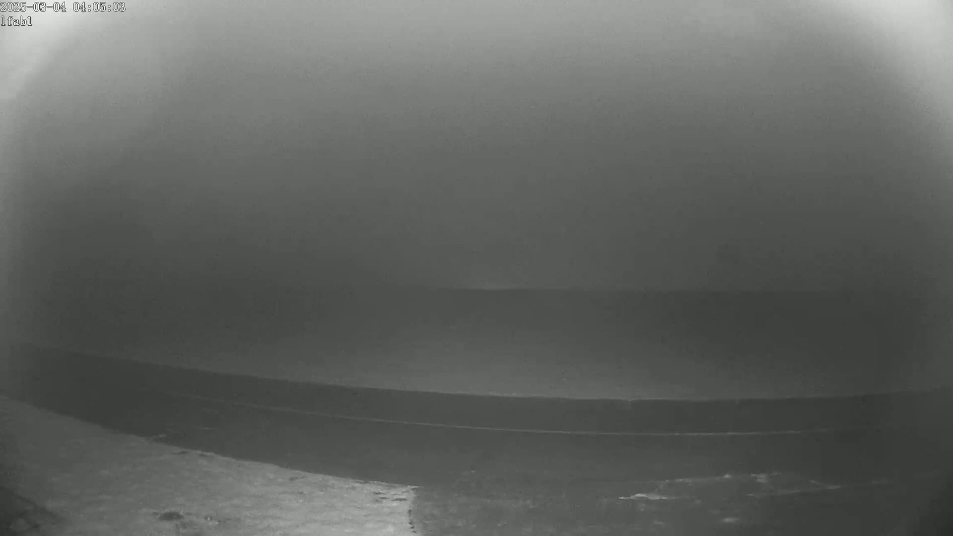 A dark, foggy scene shows a body of water with a dark shoreline in the foreground.