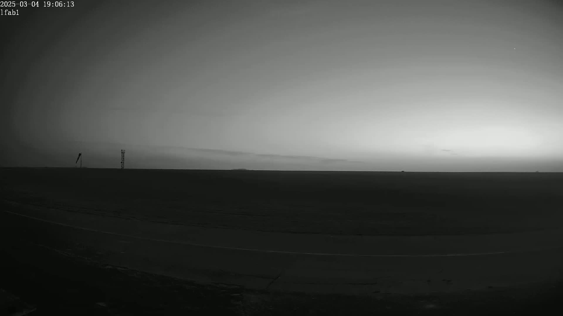A flat, dark landscape under a twilight sky shows two tall, thin structures in the distance.