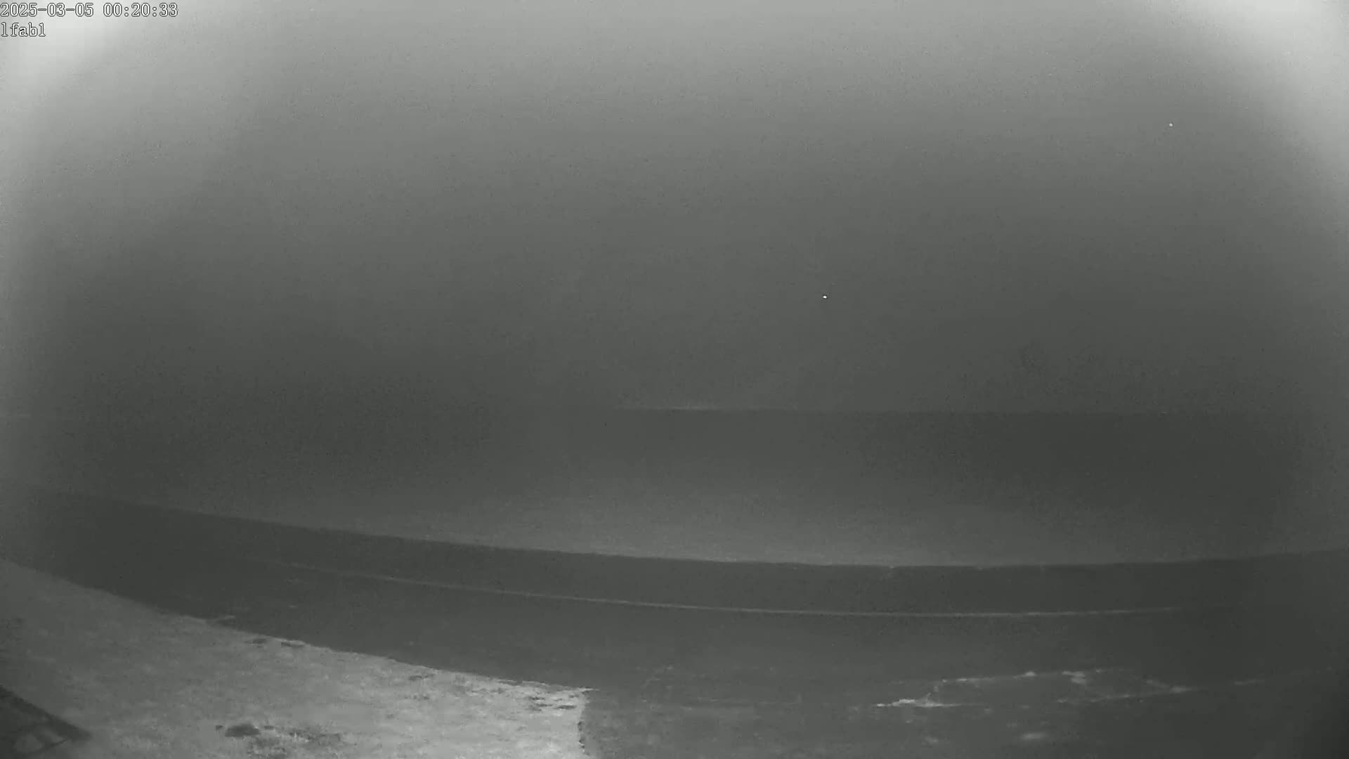 A low-light, foggy or hazy view shows a dark body of water and a slightly lighter shoreline.