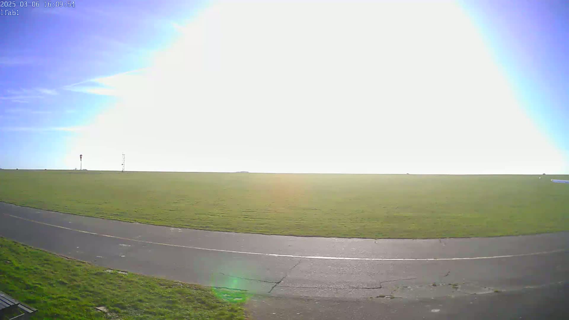 A paved path curves through a grassy field under a bright, mostly sunny sky.