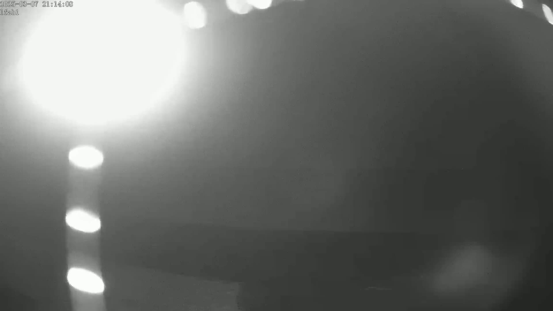 A blurry, grayscale image shows a bright light source in the upper left corner, illuminating a hazy or foggy scene.
