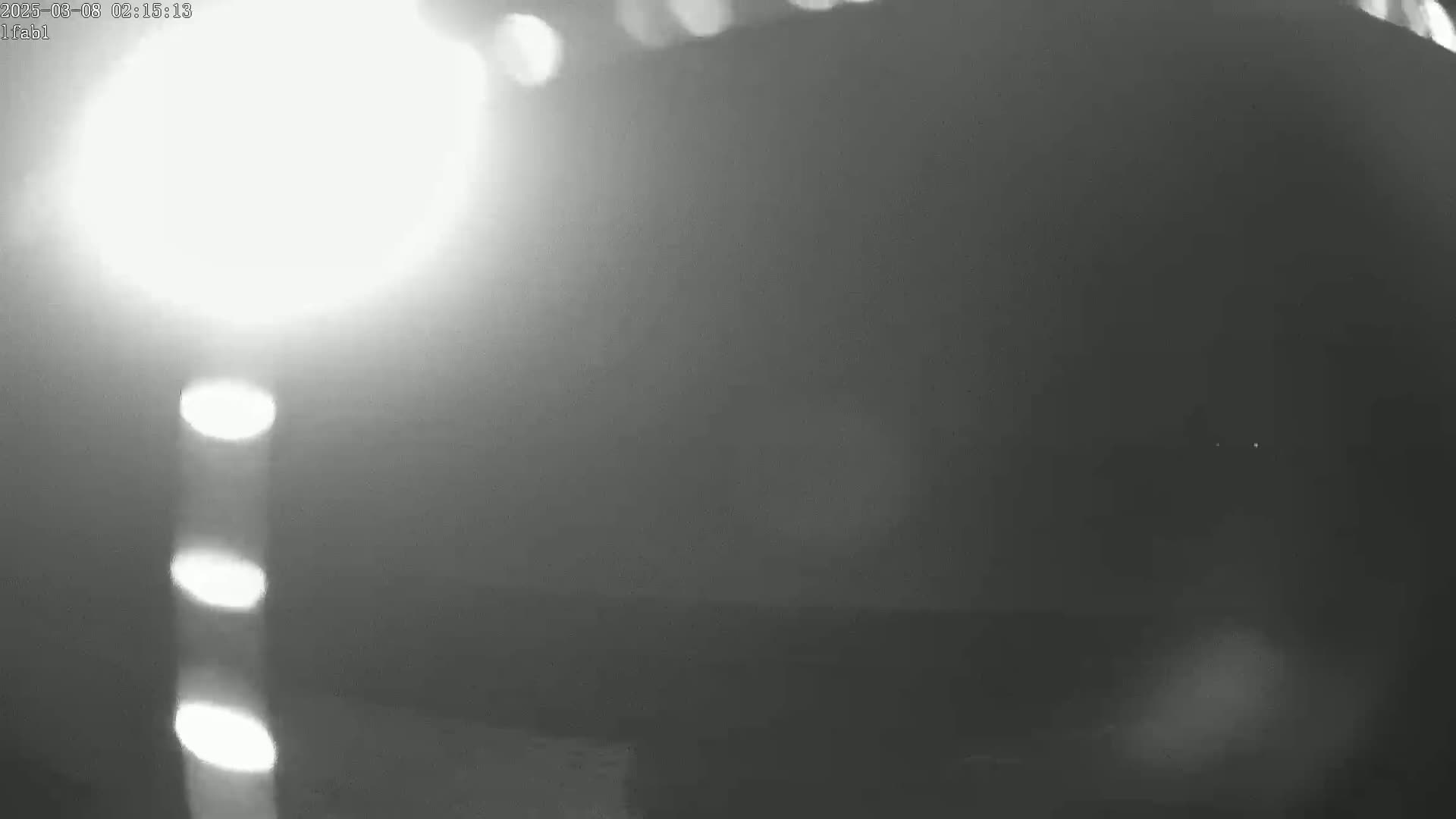 A blurry, grainy, nighttime image shows a bright light source to the left and a dark, hazy scene to the right.