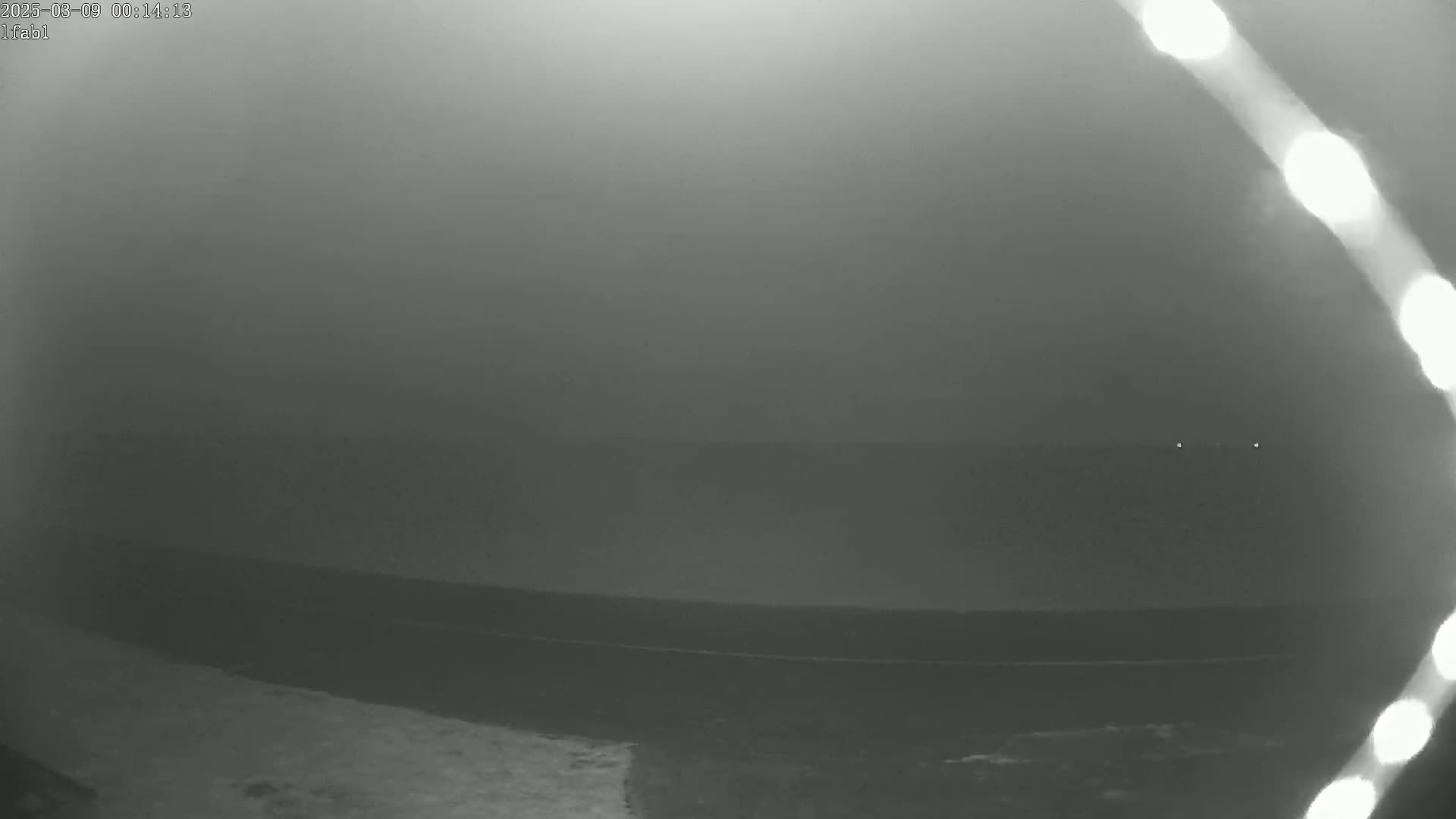 A foggy, nighttime scene shows a dark body of water with a faint shoreline and two distant lights.
