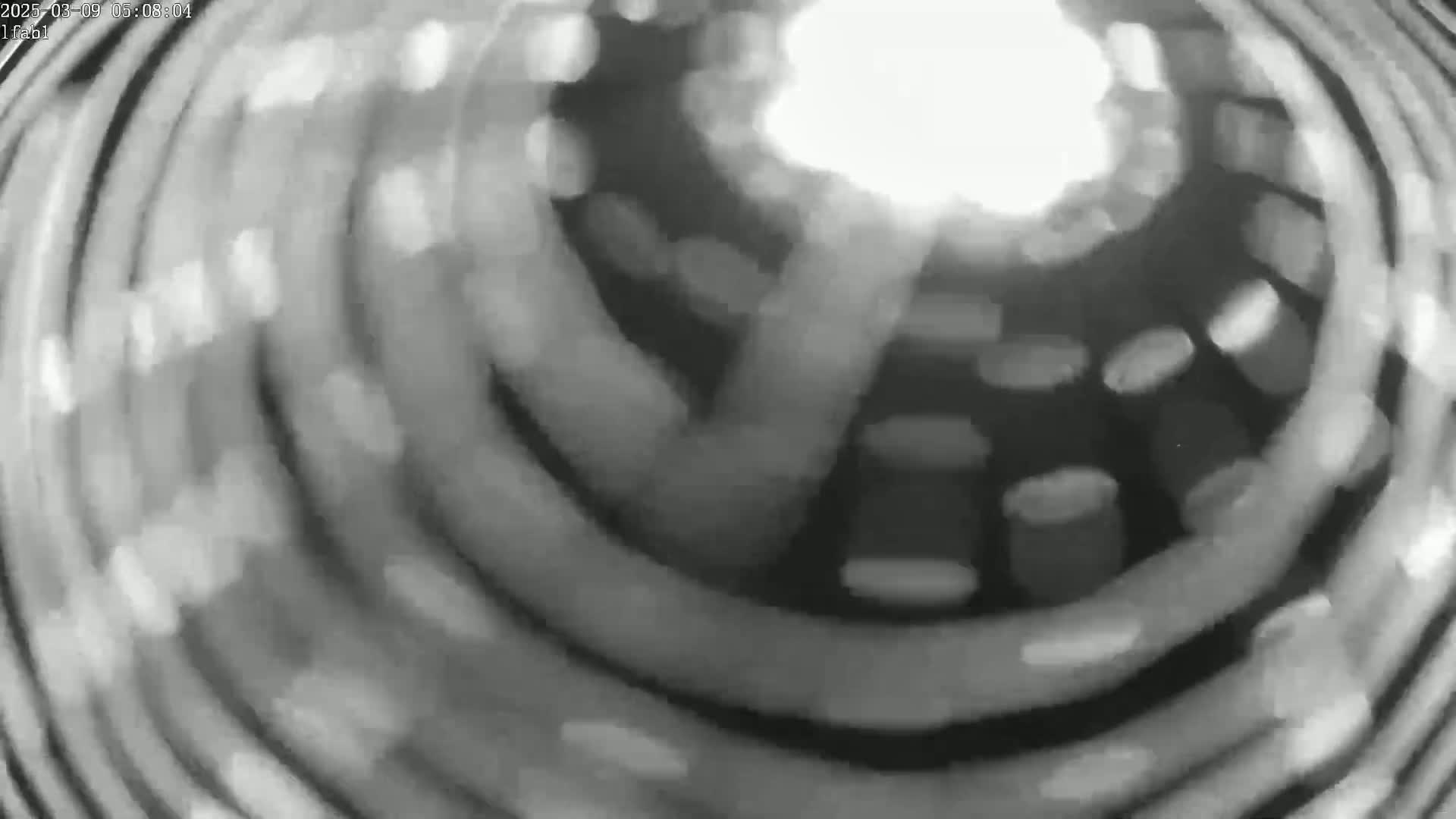 A blurry, grayscale image shows a swirling, circular pattern of light and dark shapes.