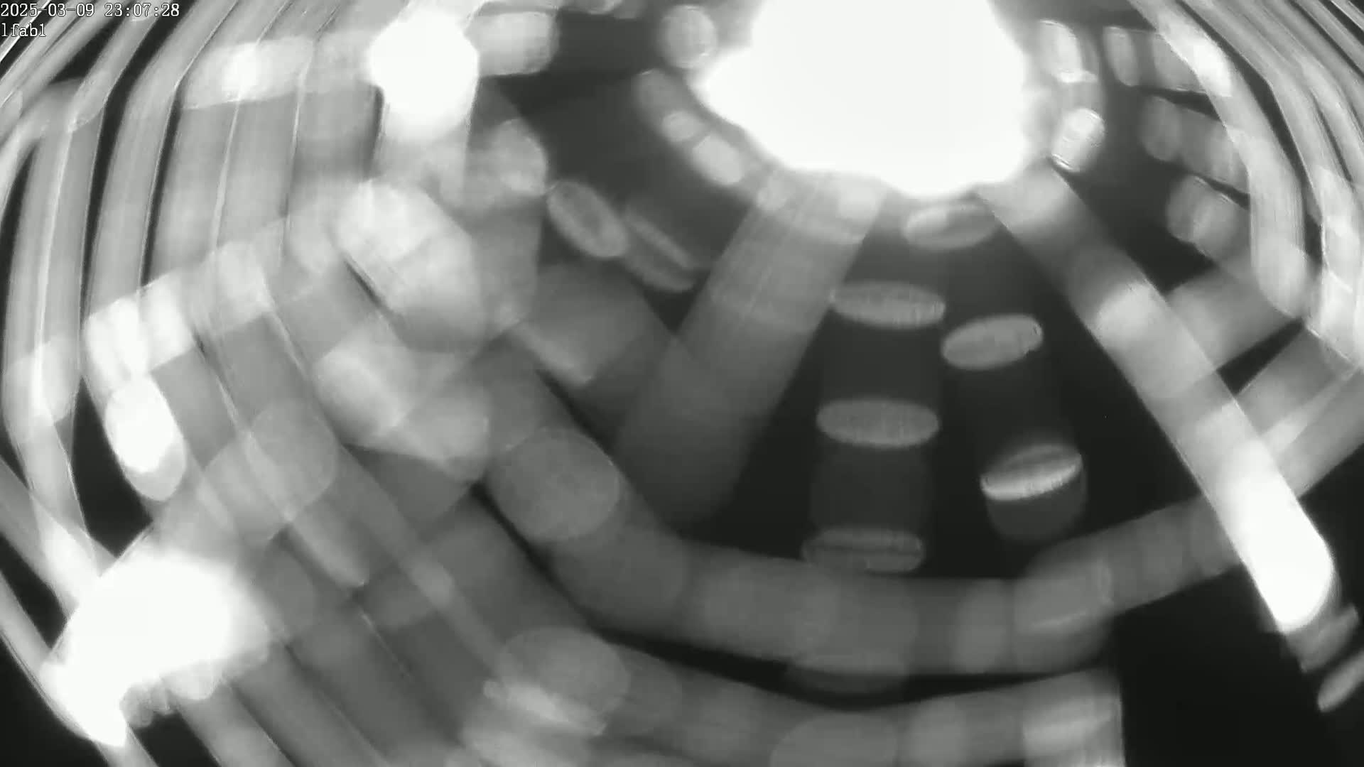 A blurry, black-and-white image shows streaks of light in a swirling motion, creating an abstract pattern.