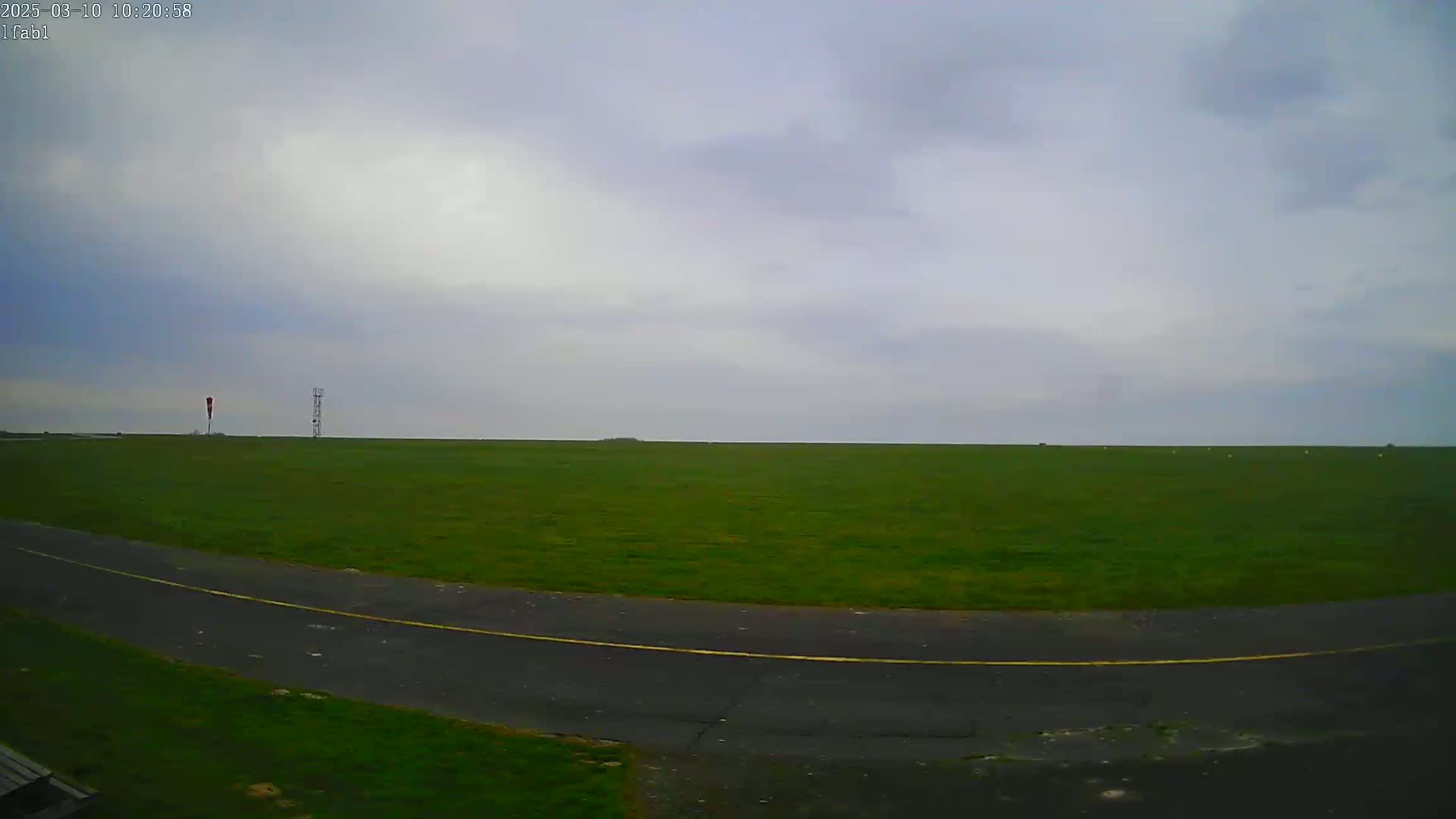 A paved road curves through a flat, grassy field under an overcast sky.