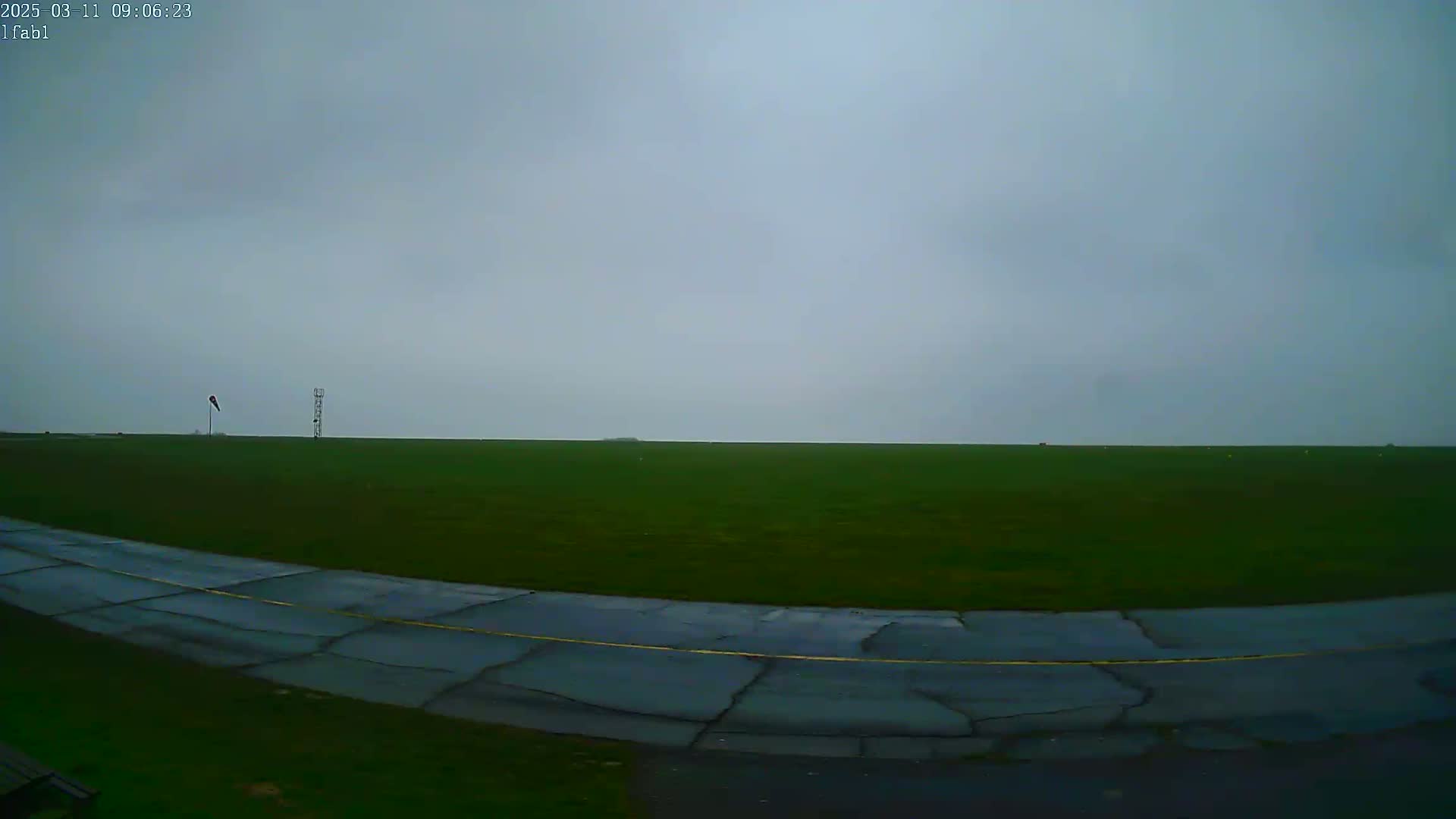 A mostly overcast sky hangs over a flat, green field with a cracked asphalt roadway curving into the foreground.