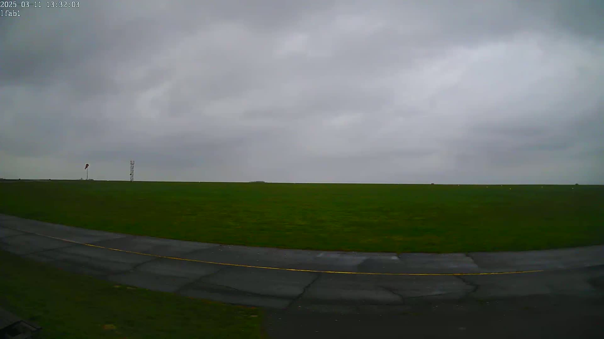 A grassy airfield with a paved taxiway curves into view under an overcast sky.