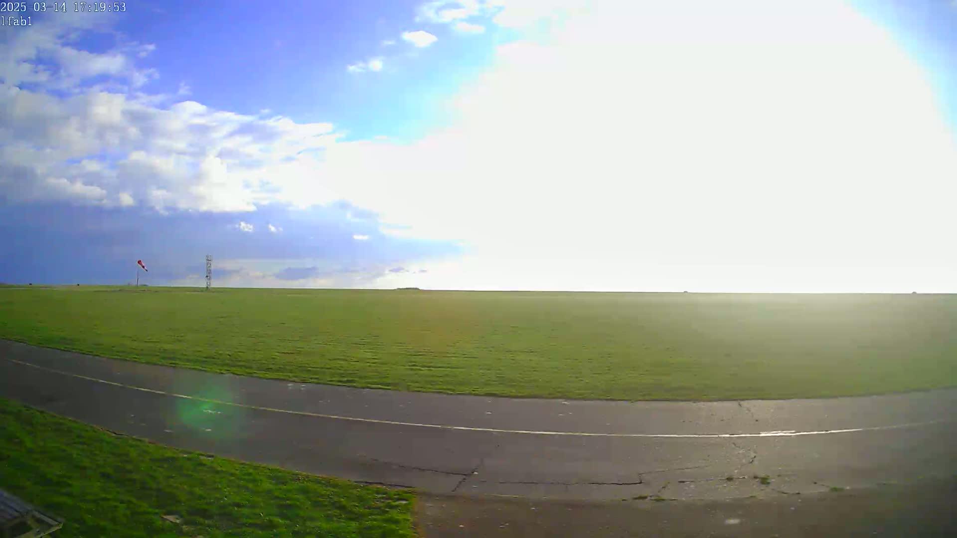 A grassy field with a paved road curves into the foreground under a partly cloudy sky.