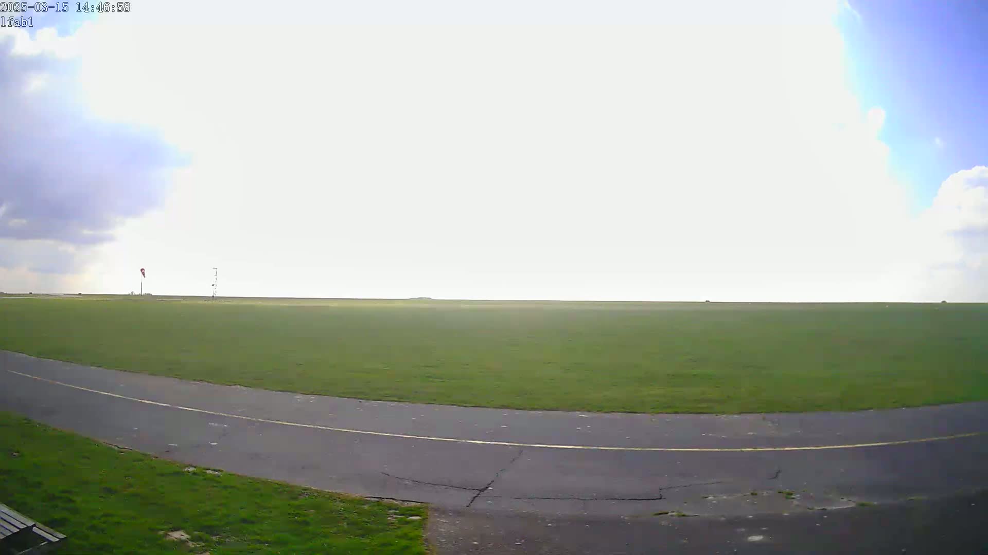 A partly cloudy sky overlooks a grassy field with a paved road curving through it.