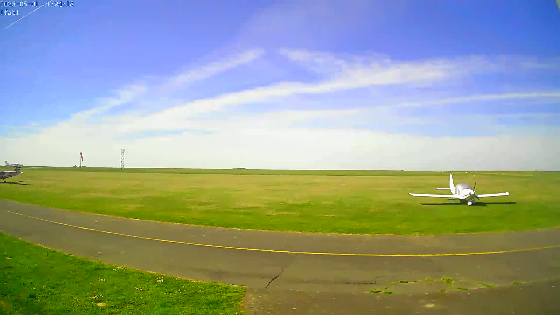 A small white airplane sits on a grassy airfield under a mostly clear blue sky.