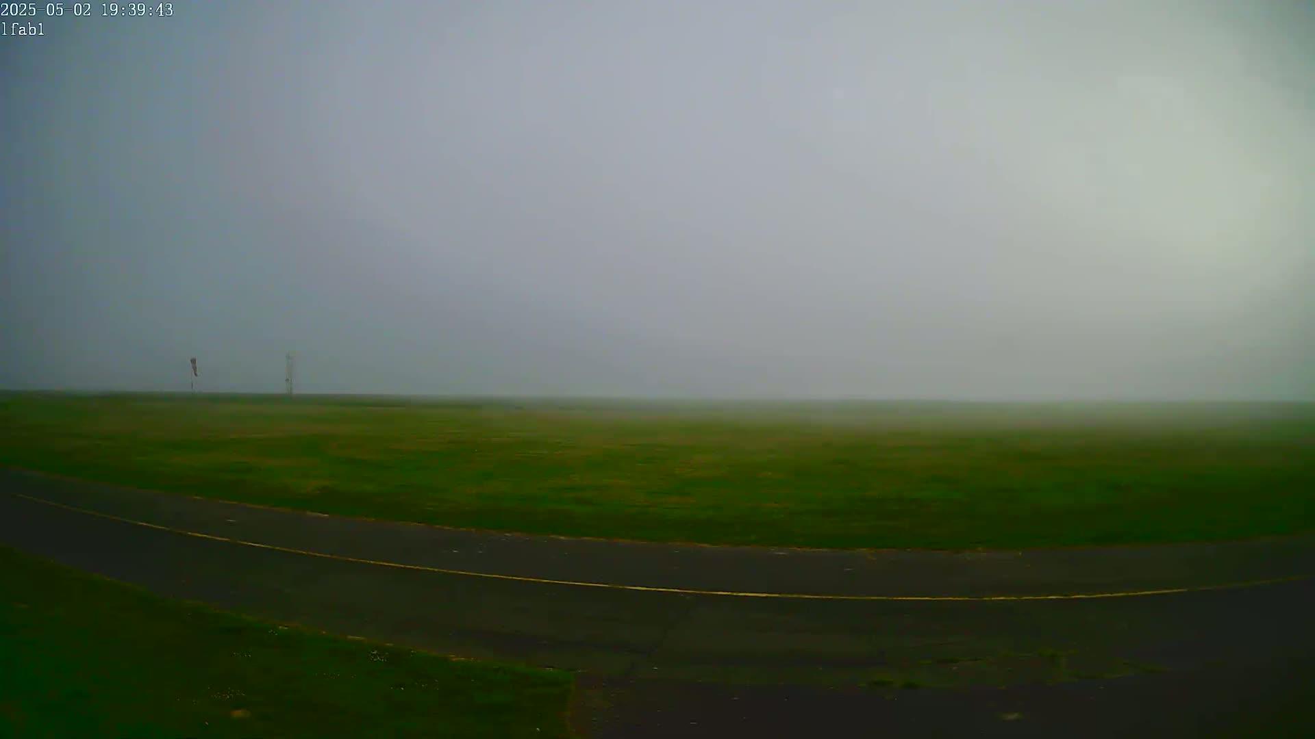 A foggy field with a paved road curving through it, and two tall objects in the distance.
