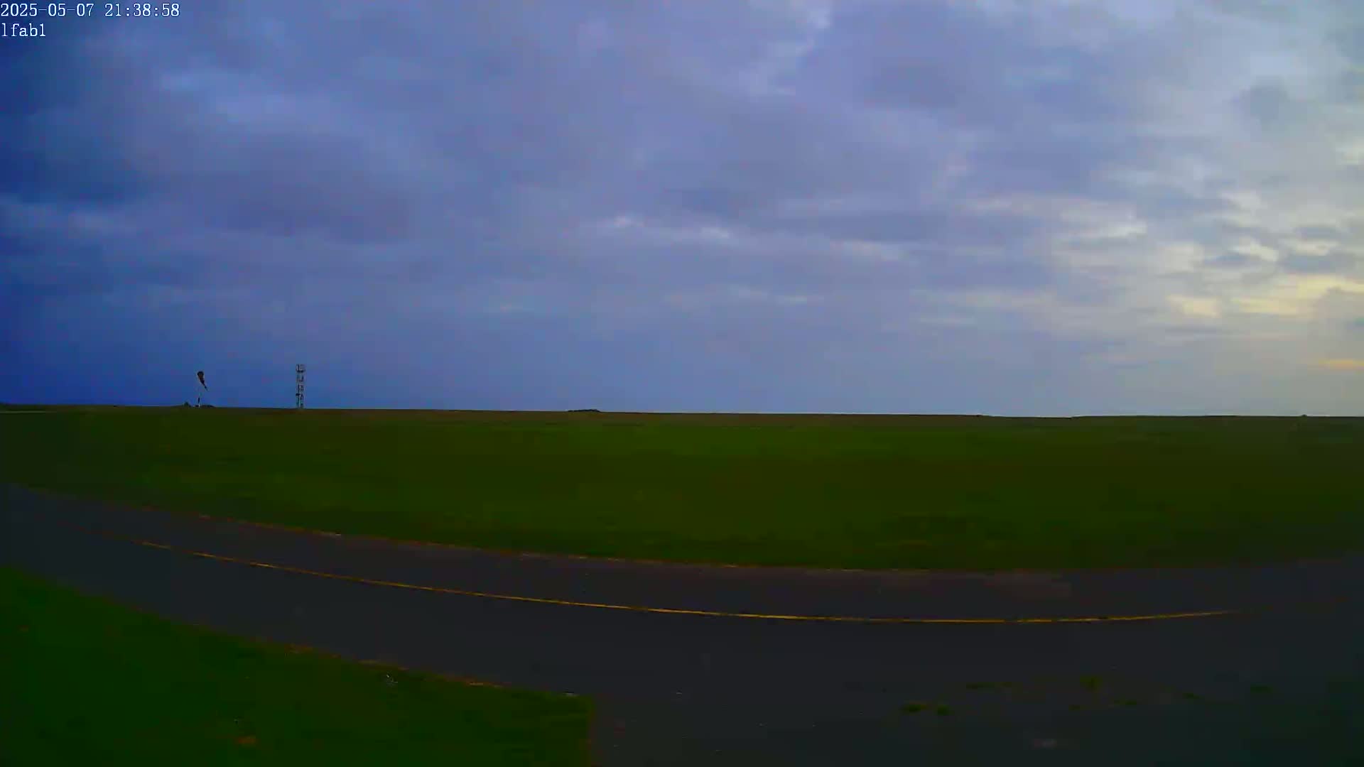 A paved road curves through a flat, grassy field under a mostly cloudy, dusky sky.