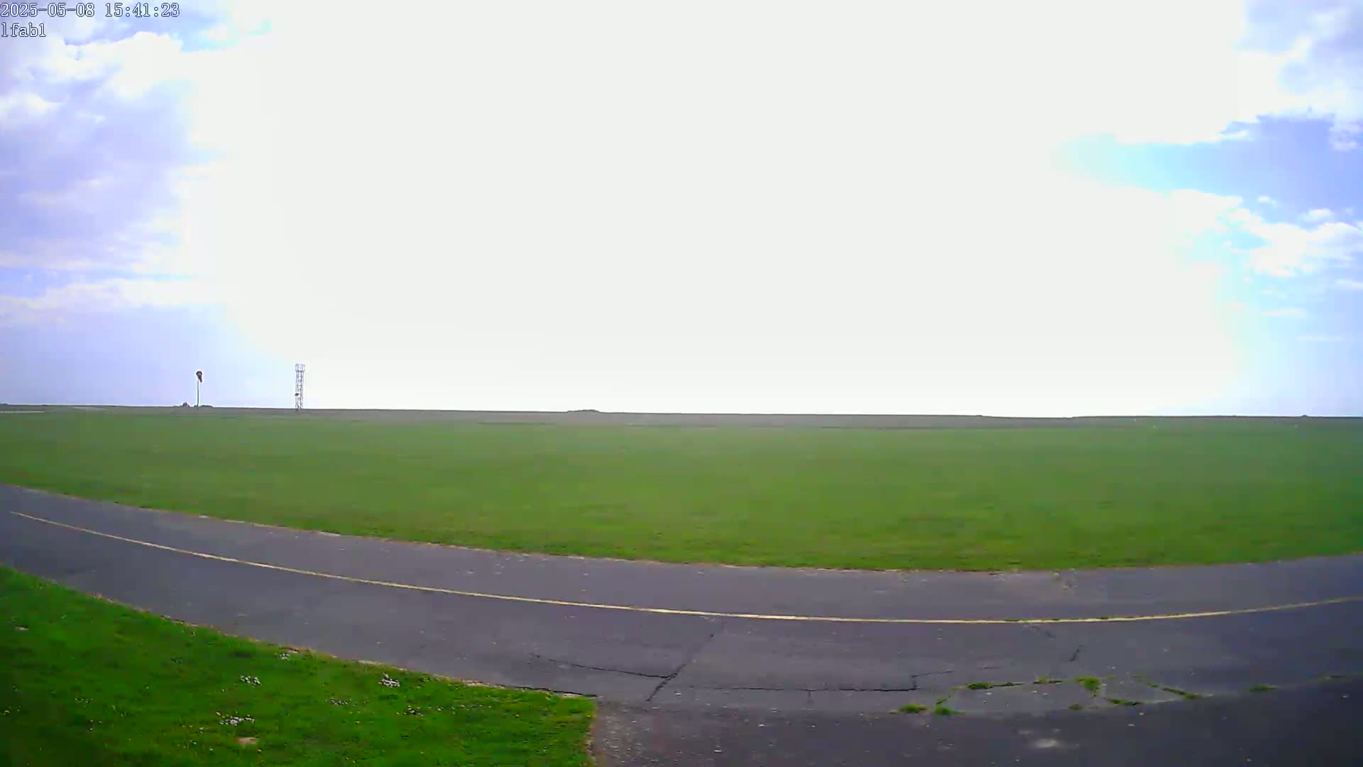 A paved road curves through a large, grassy field under a partly cloudy sky.
