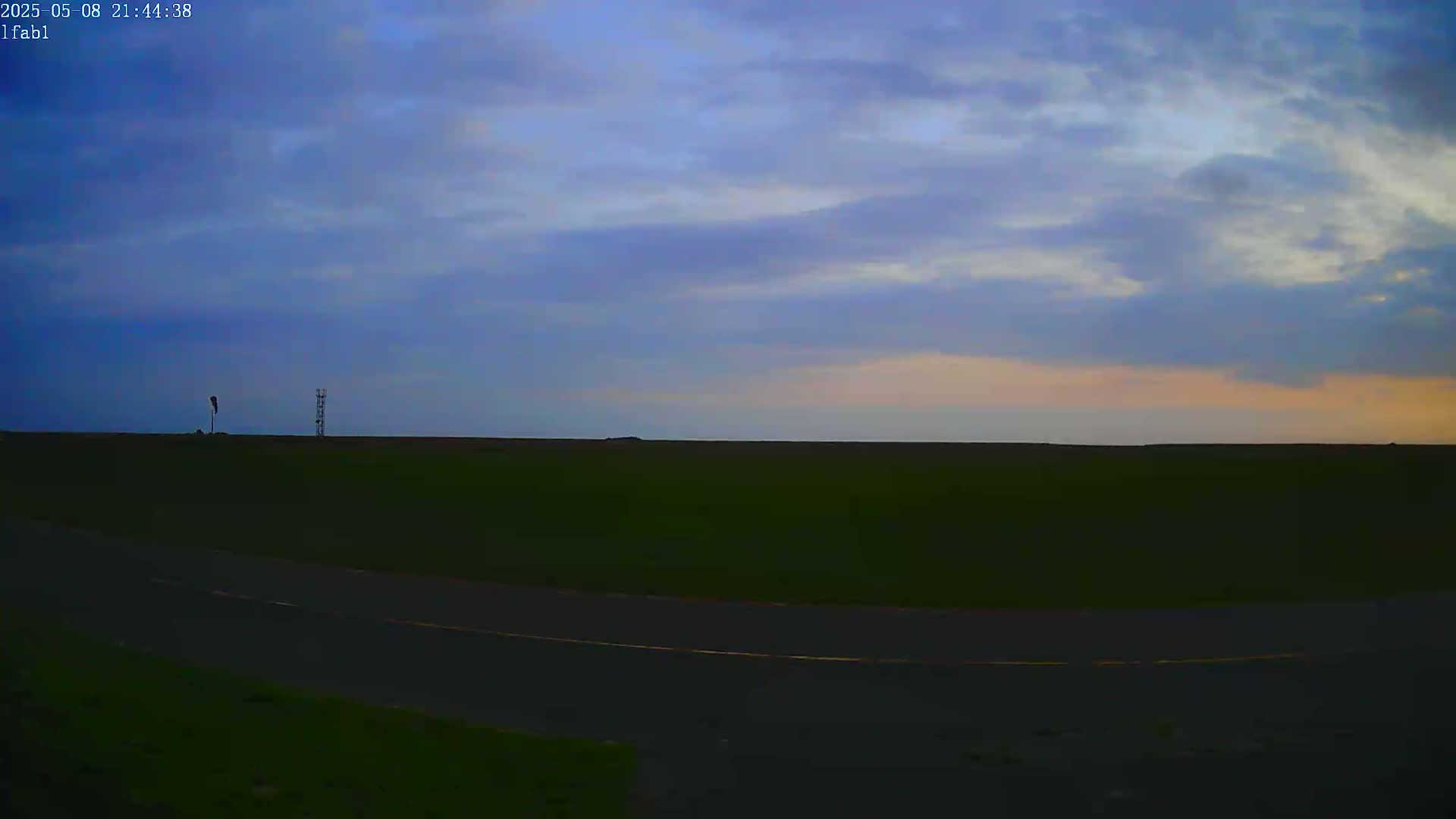 A flat, dark green field stretches to a pale horizon under a twilight sky filled with mostly cloudy, purplish-blue hues.