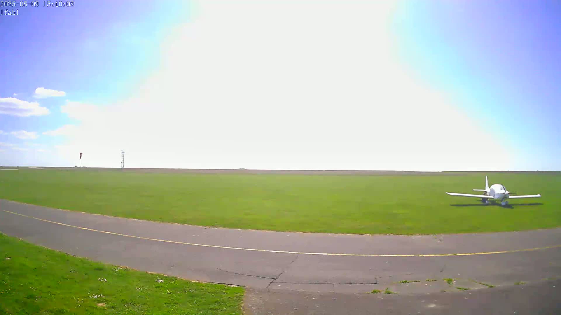 A small white airplane sits on a grassy airfield under a mostly sunny sky.