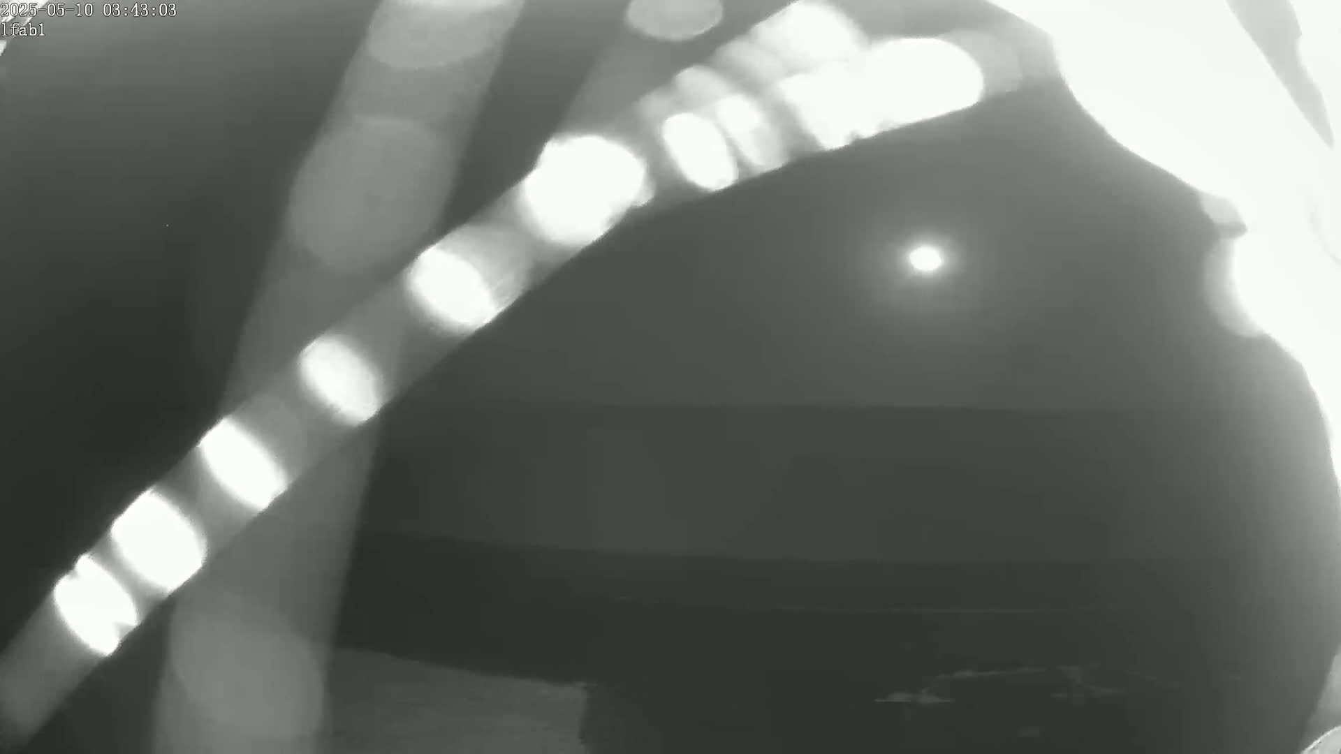 A low-resolution grayscale image shows a bright sun setting behind a dark, indistinct landscape, partially obscured by bright streaks of light.