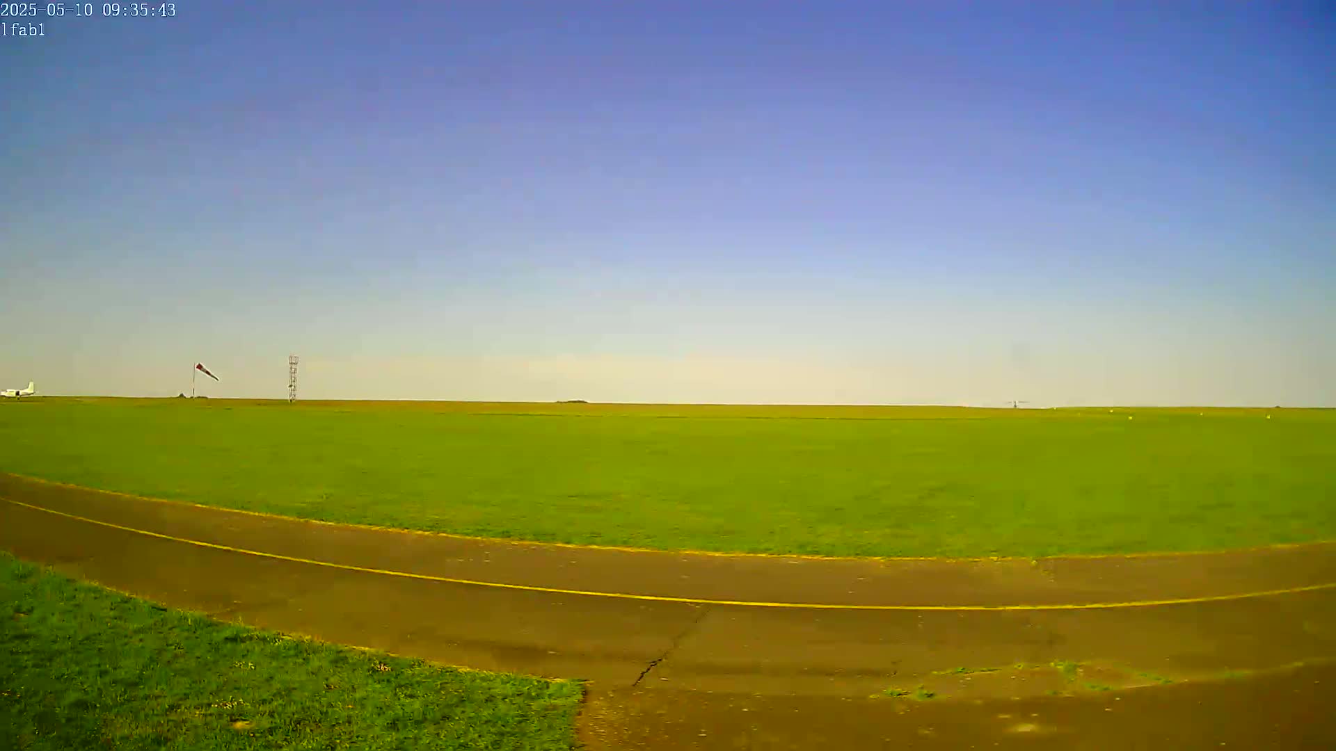 A small airplane sits on a grassy airfield under a clear blue sky.