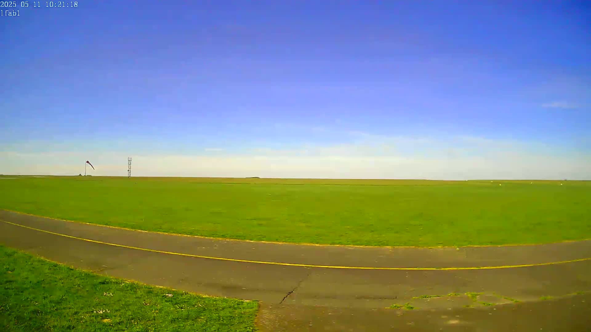 A paved path curves through a large, grassy field under a clear blue sky.
