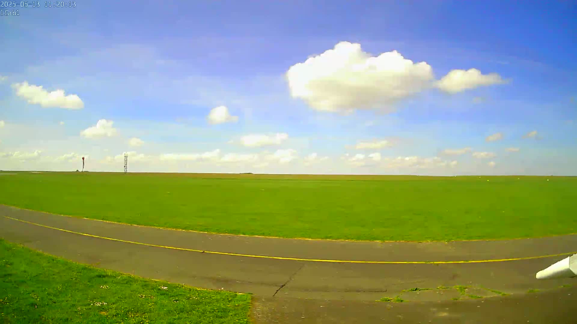 A paved path curves through a grassy field under a partly cloudy blue sky.