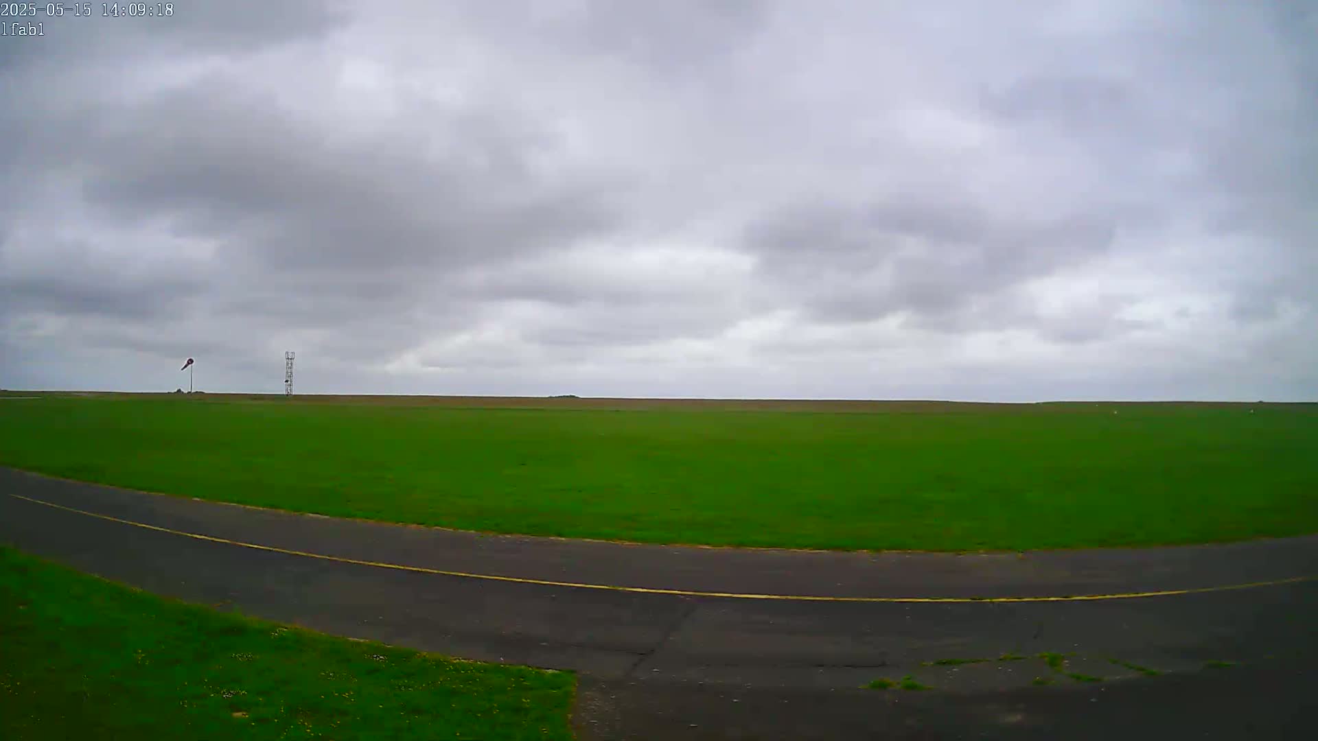 A paved road curves through a large, grassy field under an overcast sky.