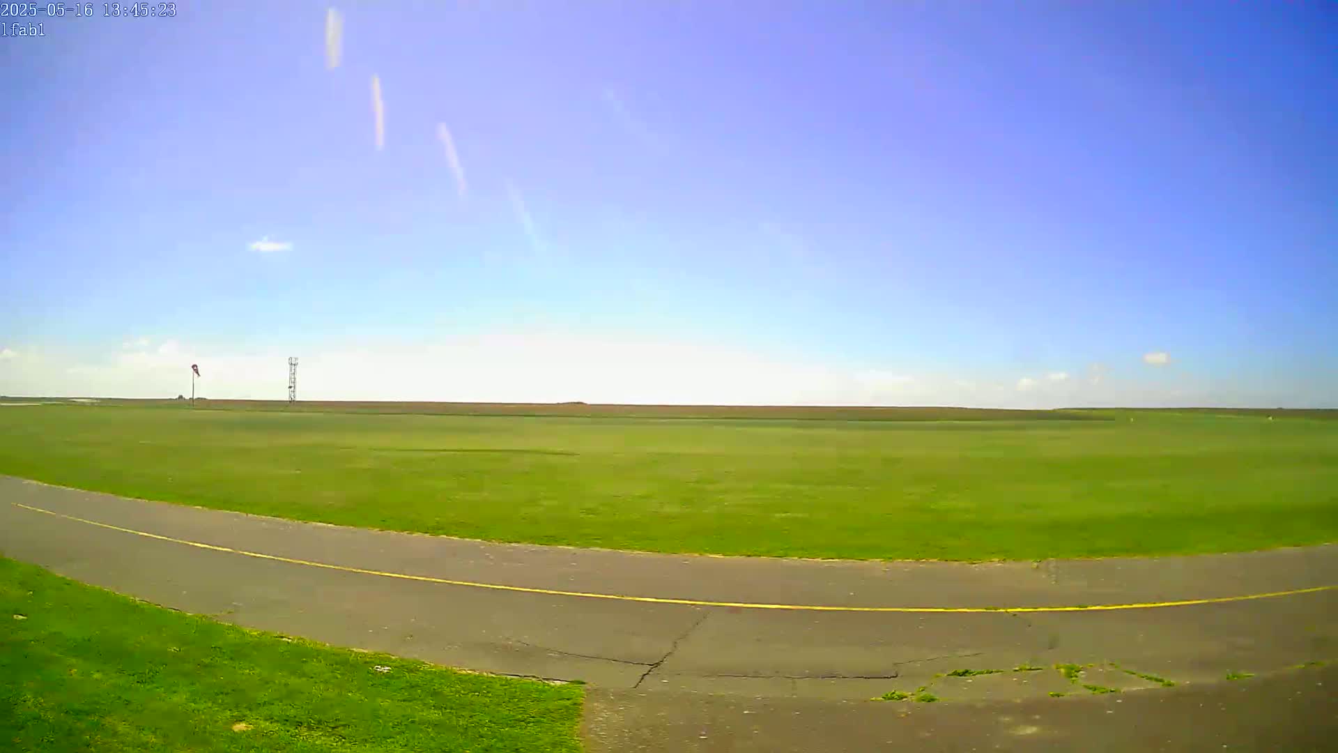 A paved path curves through a large, grassy field under a clear blue sky.