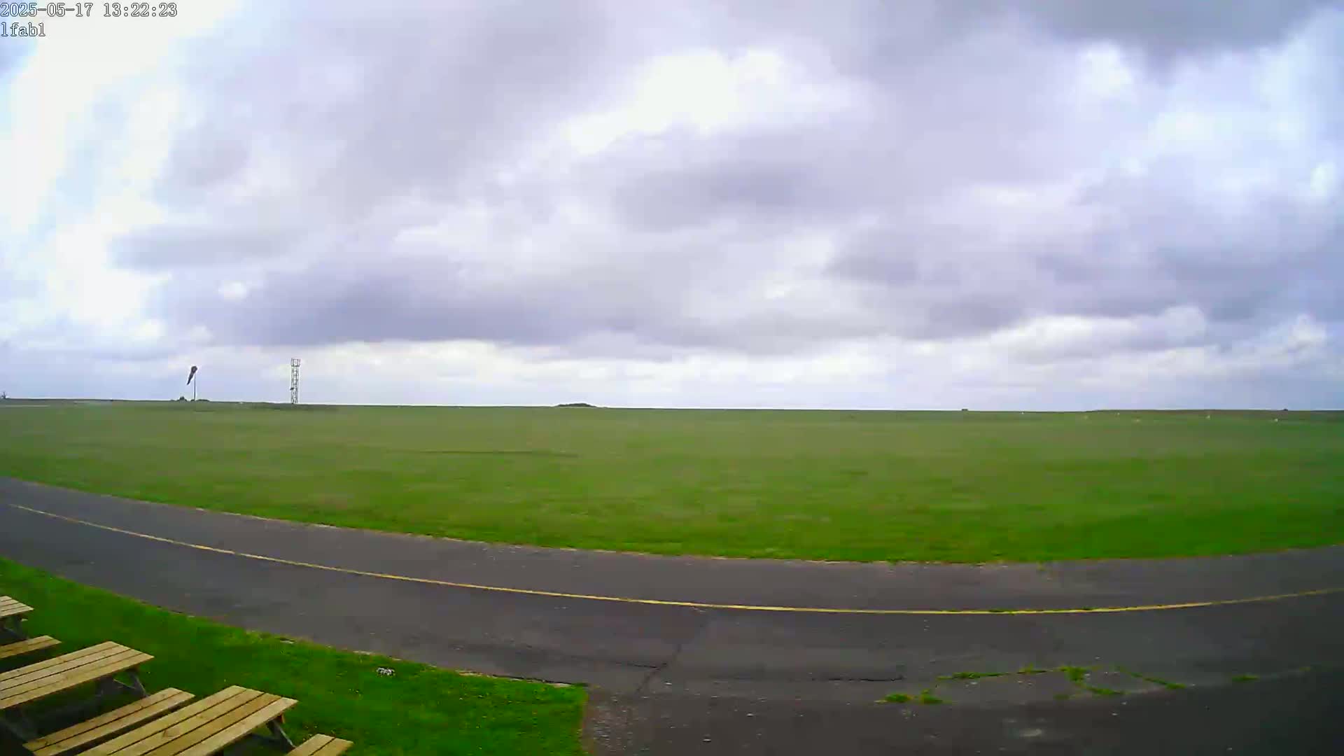 A grassy field with a paved road curves around the bottom, under an overcast sky.