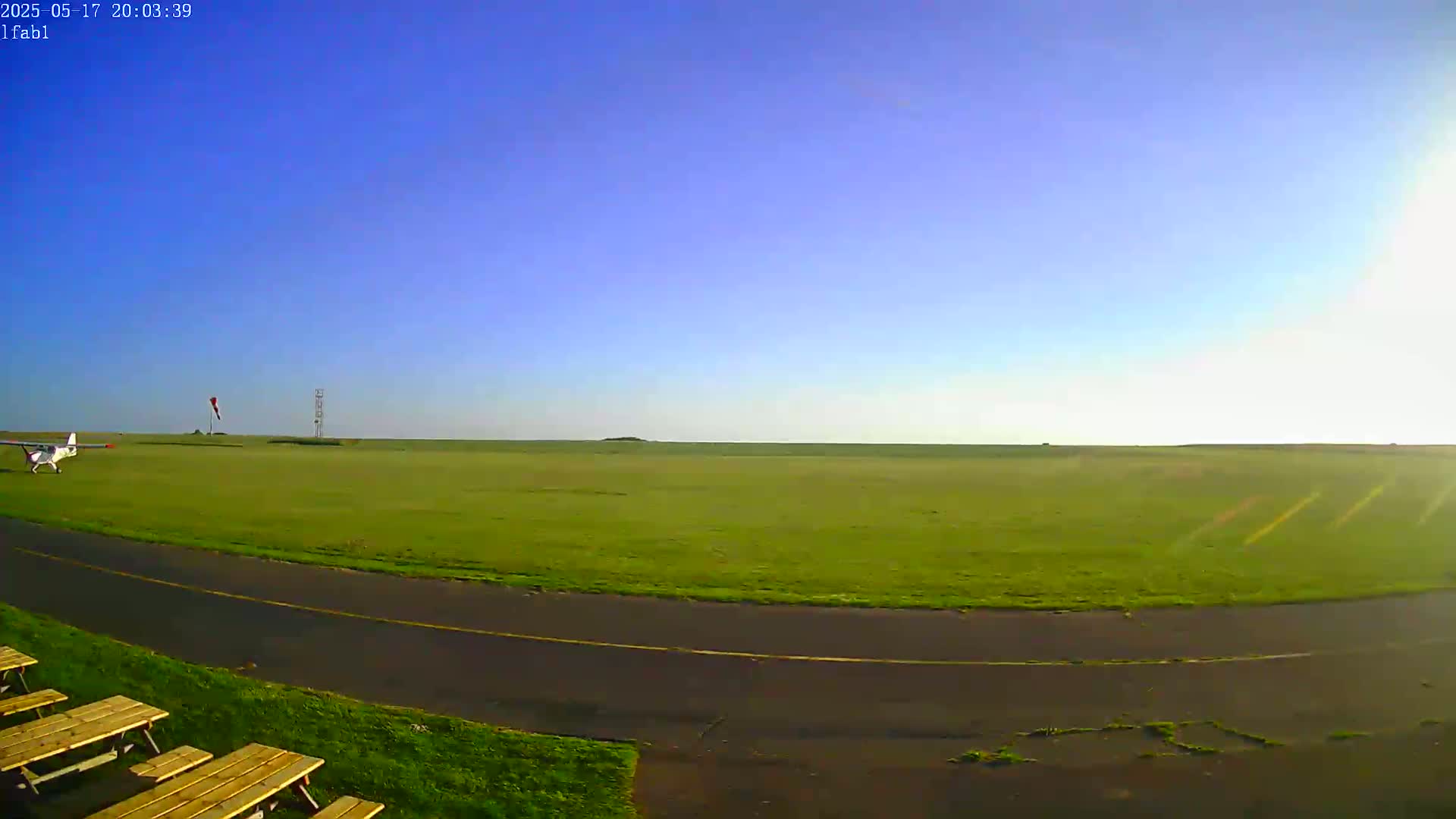 A small airplane sits on a grassy airfield under a clear blue sky.