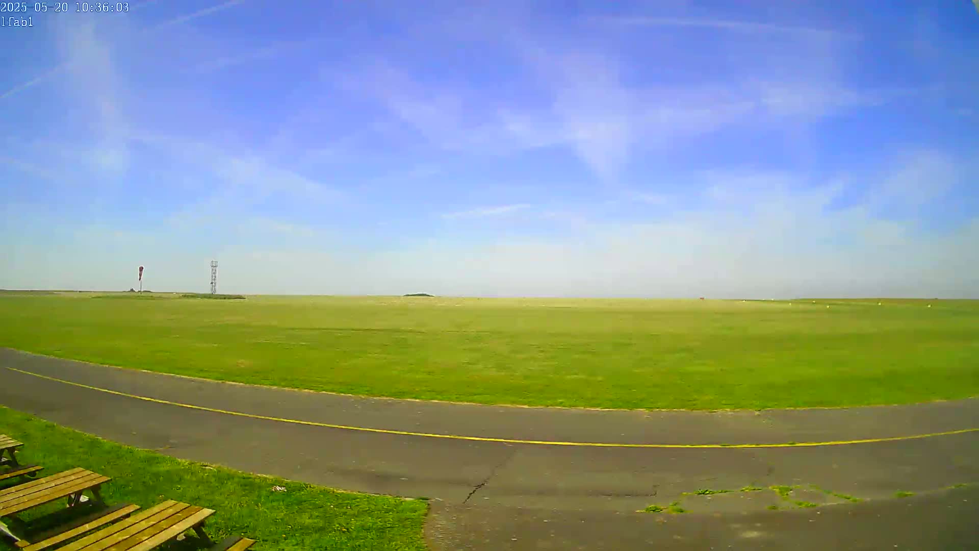 A paved path curves through a grassy field under a mostly clear blue sky.