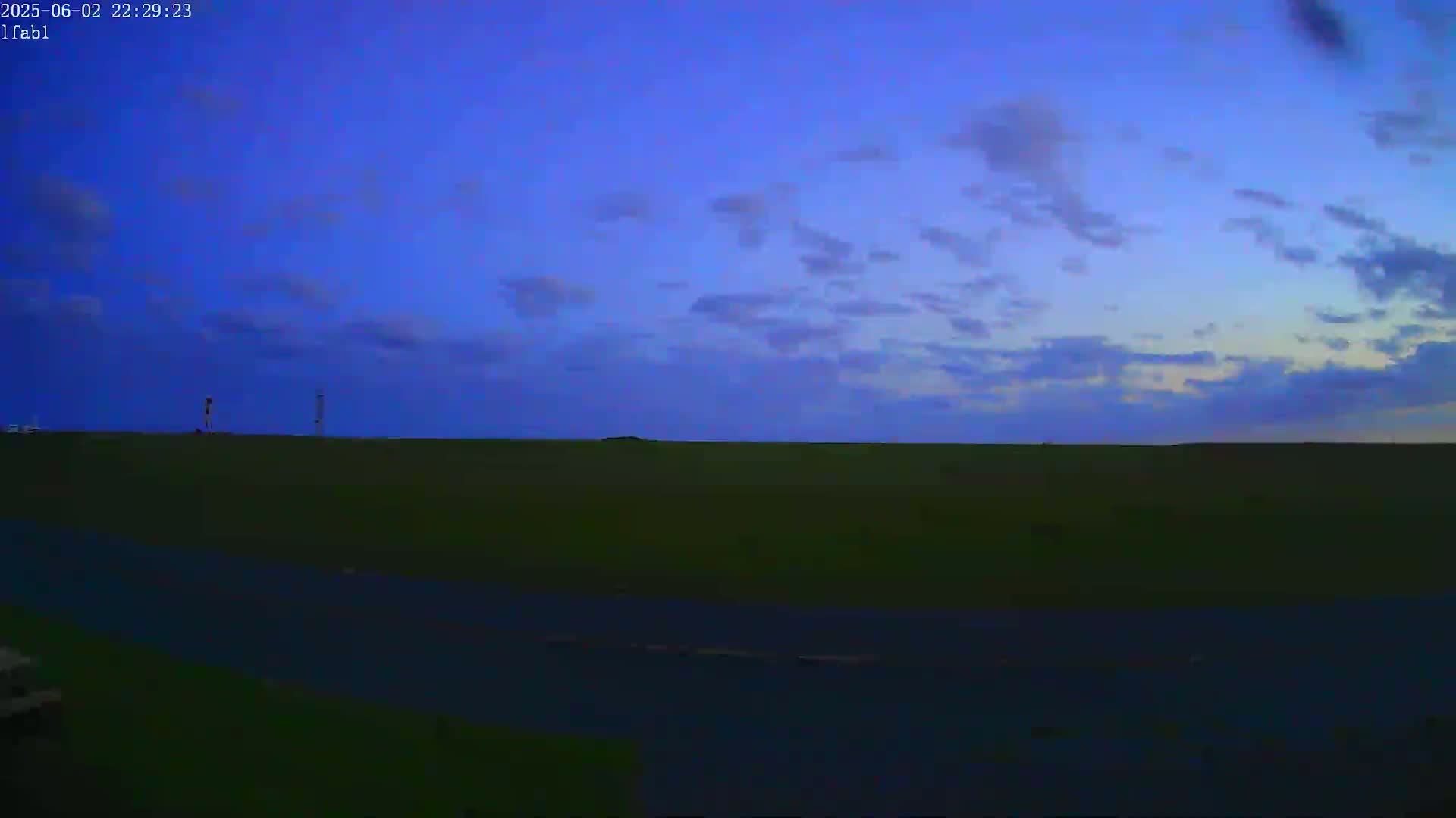 A flat, dark green field stretches to a twilight sky filled with thin, wispy clouds.
