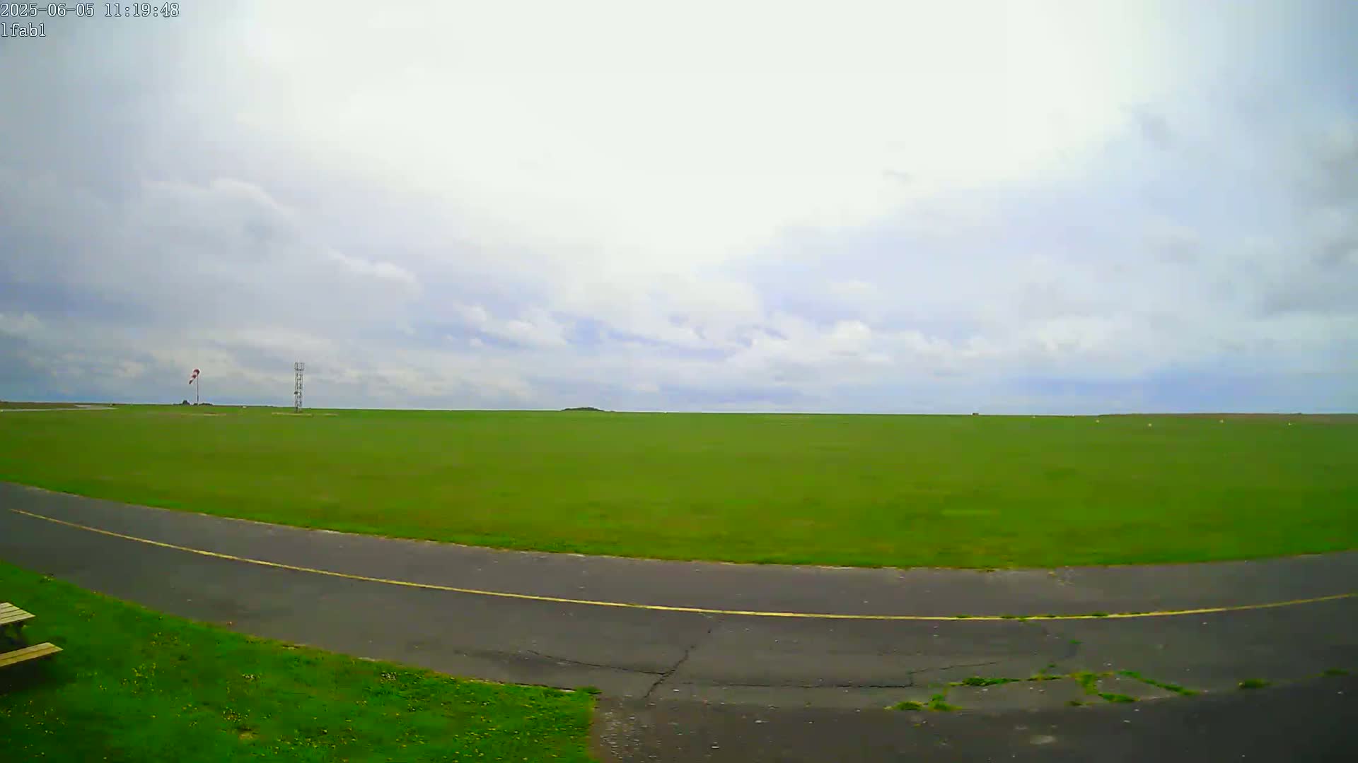 A vast green field with a paved road curving through it under a partly cloudy sky.