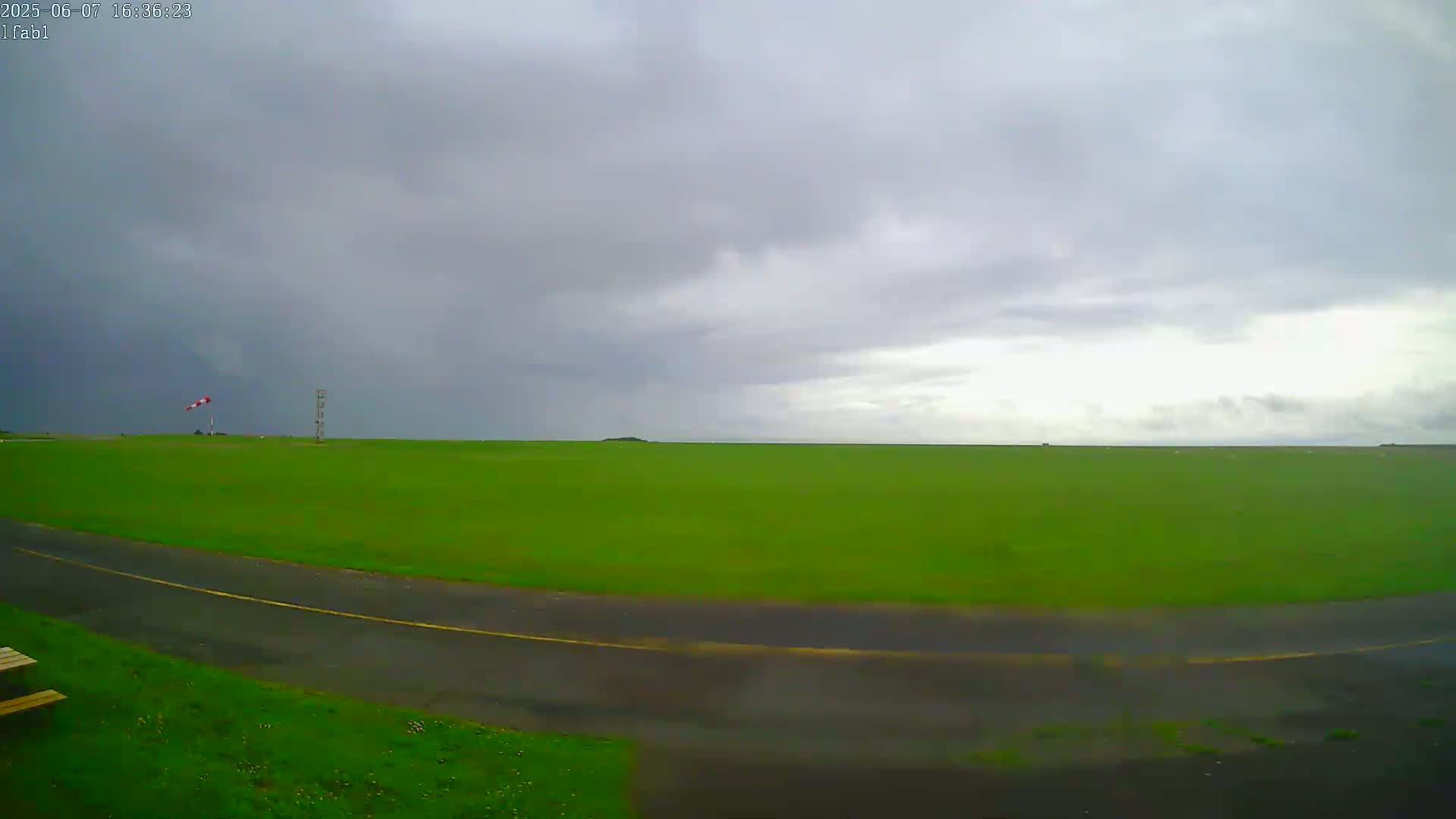 A vast green field stretches to the horizon under a mostly cloudy sky.