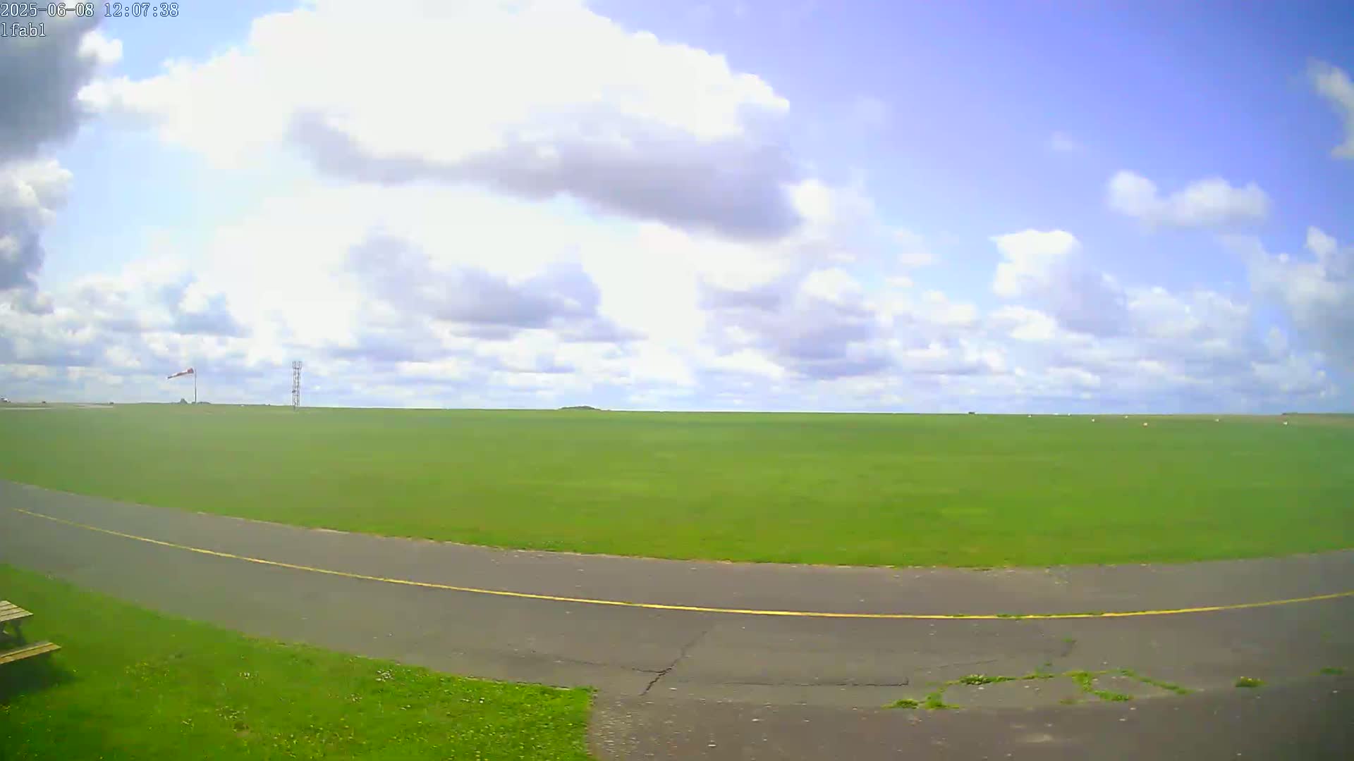 A wide, grassy field under a partly cloudy sky, with a paved road curving through the foreground.