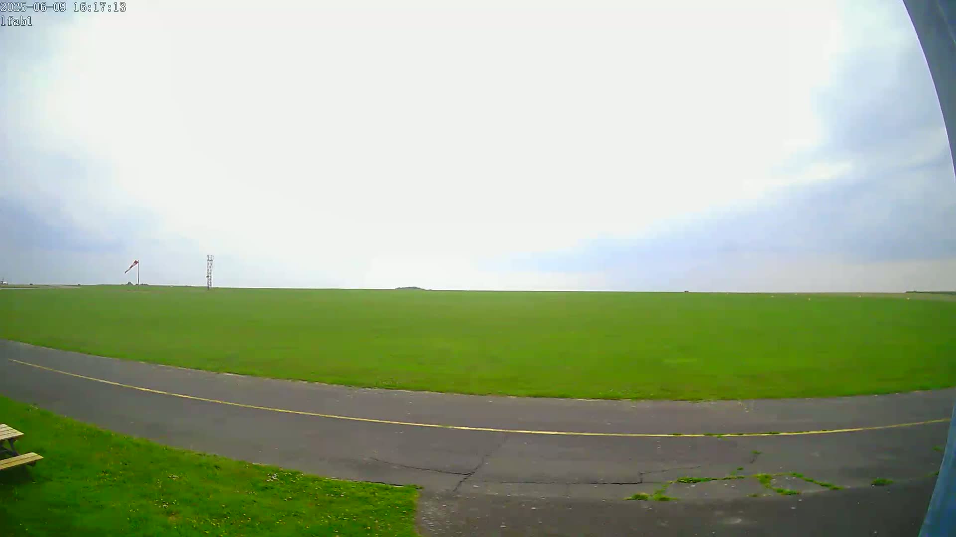 A grassy airfield with a paved road curving through it is seen under an overcast sky.