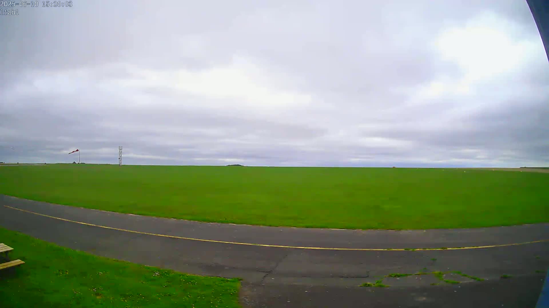 A wide expanse of bright green grass, a paved road curving through it, and an overcast sky are visible.