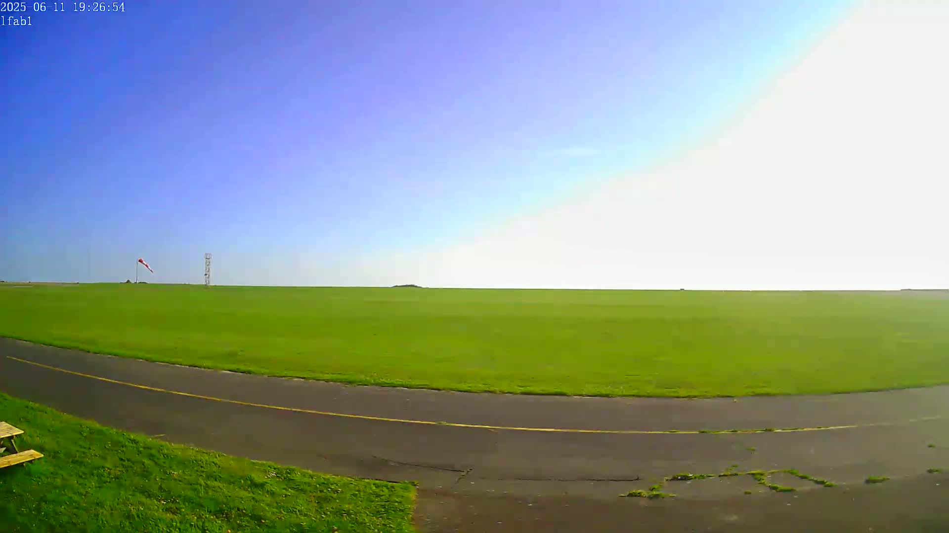 A grassy airfield under a clear blue sky with a windsock and tower visible in the distance.
