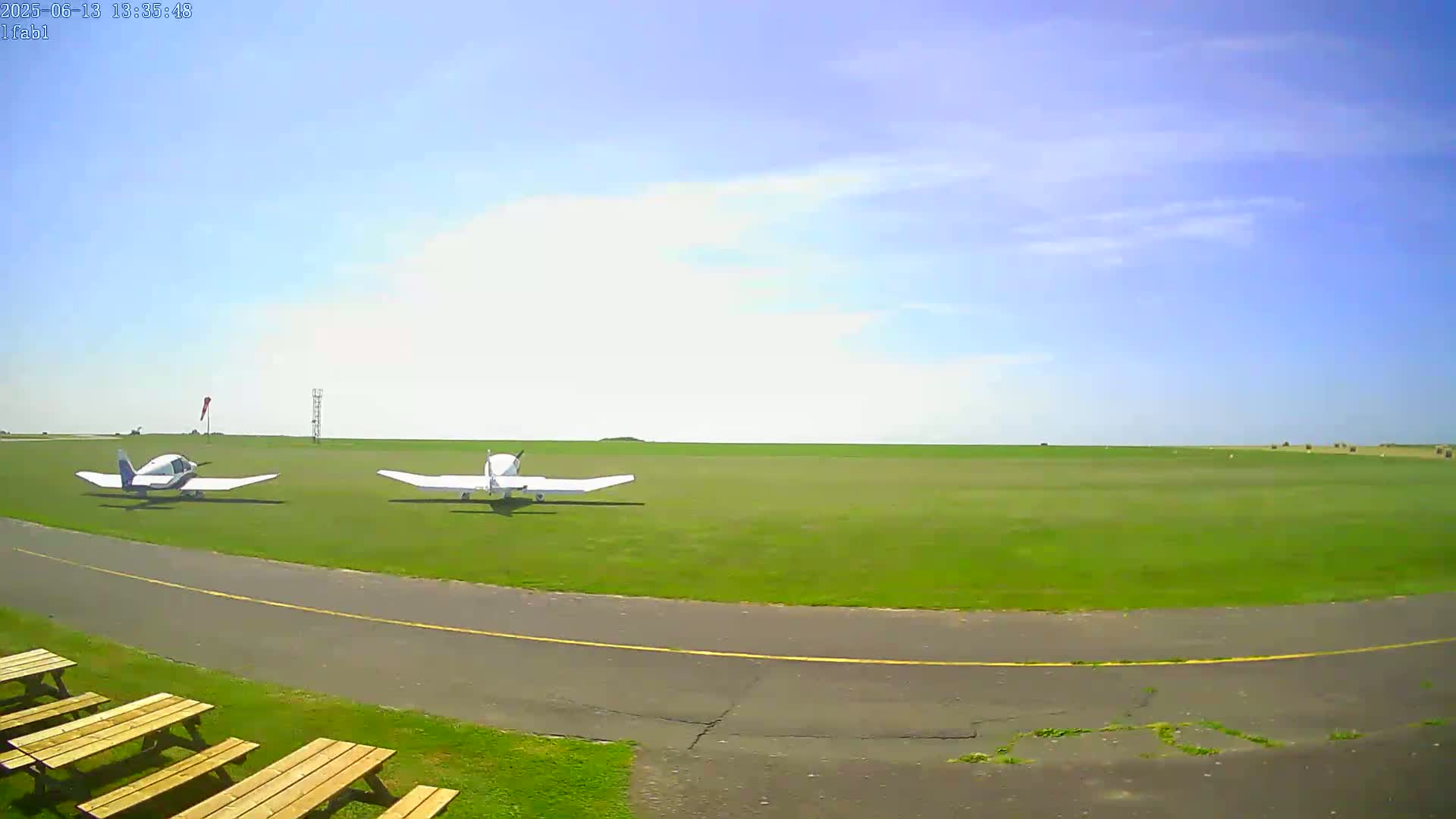 Two small, white airplanes are parked on a grassy airfield under a mostly clear blue sky.