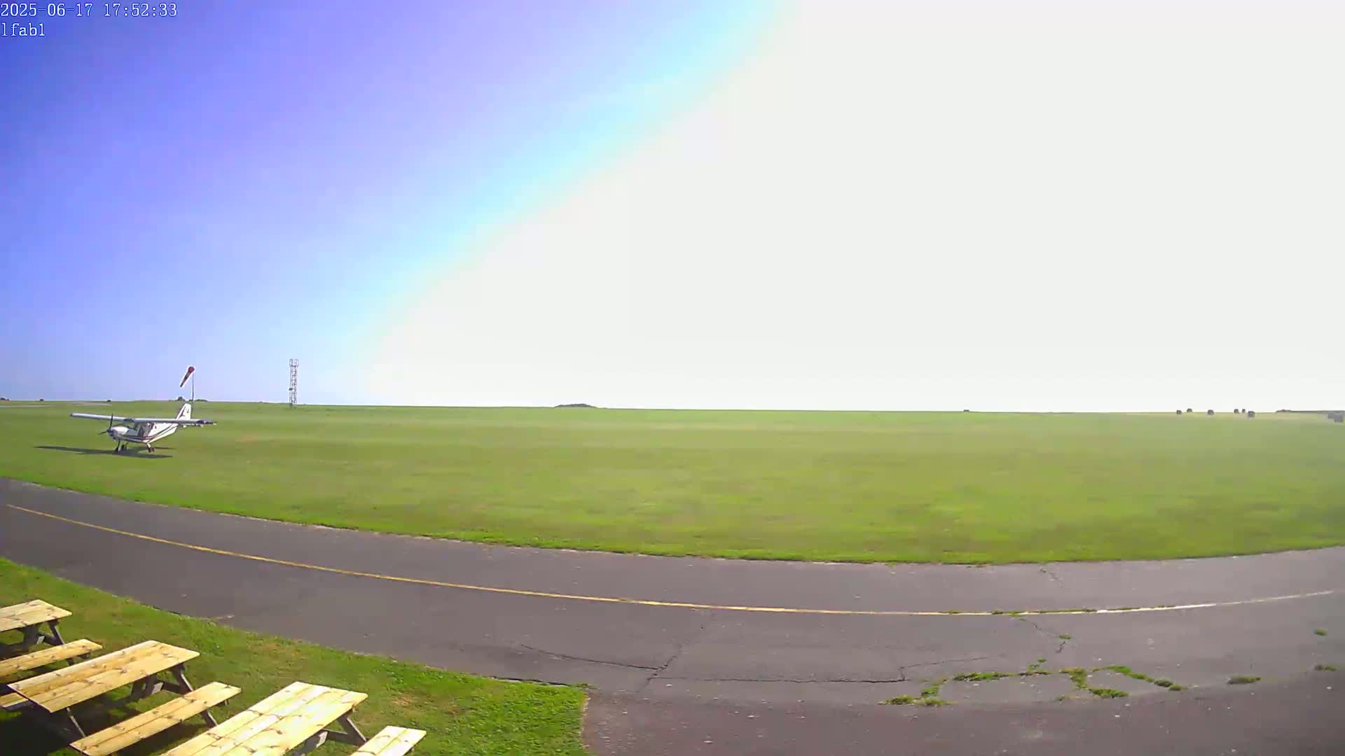 A small airplane sits on a grassy airfield under a mostly clear, bright sky.