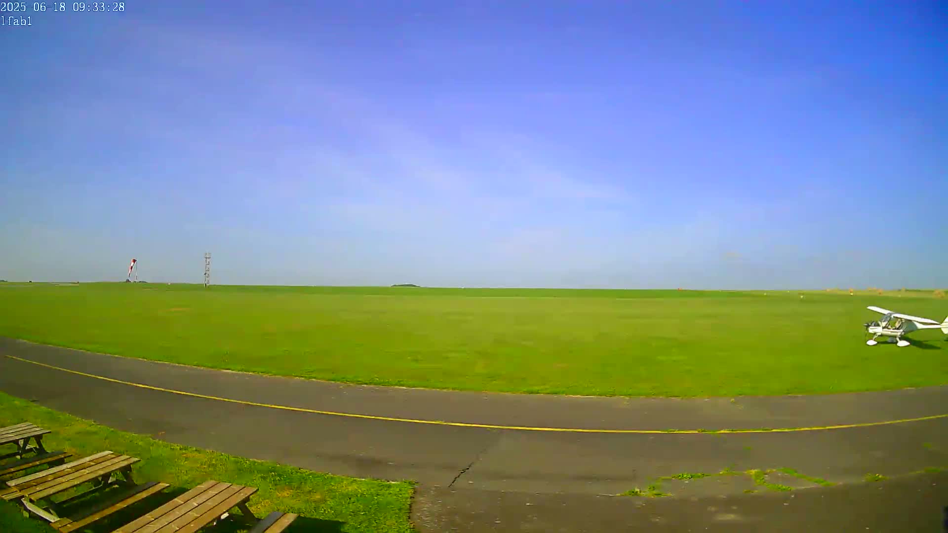 A small white airplane sits on a grassy airfield under a clear blue sky.