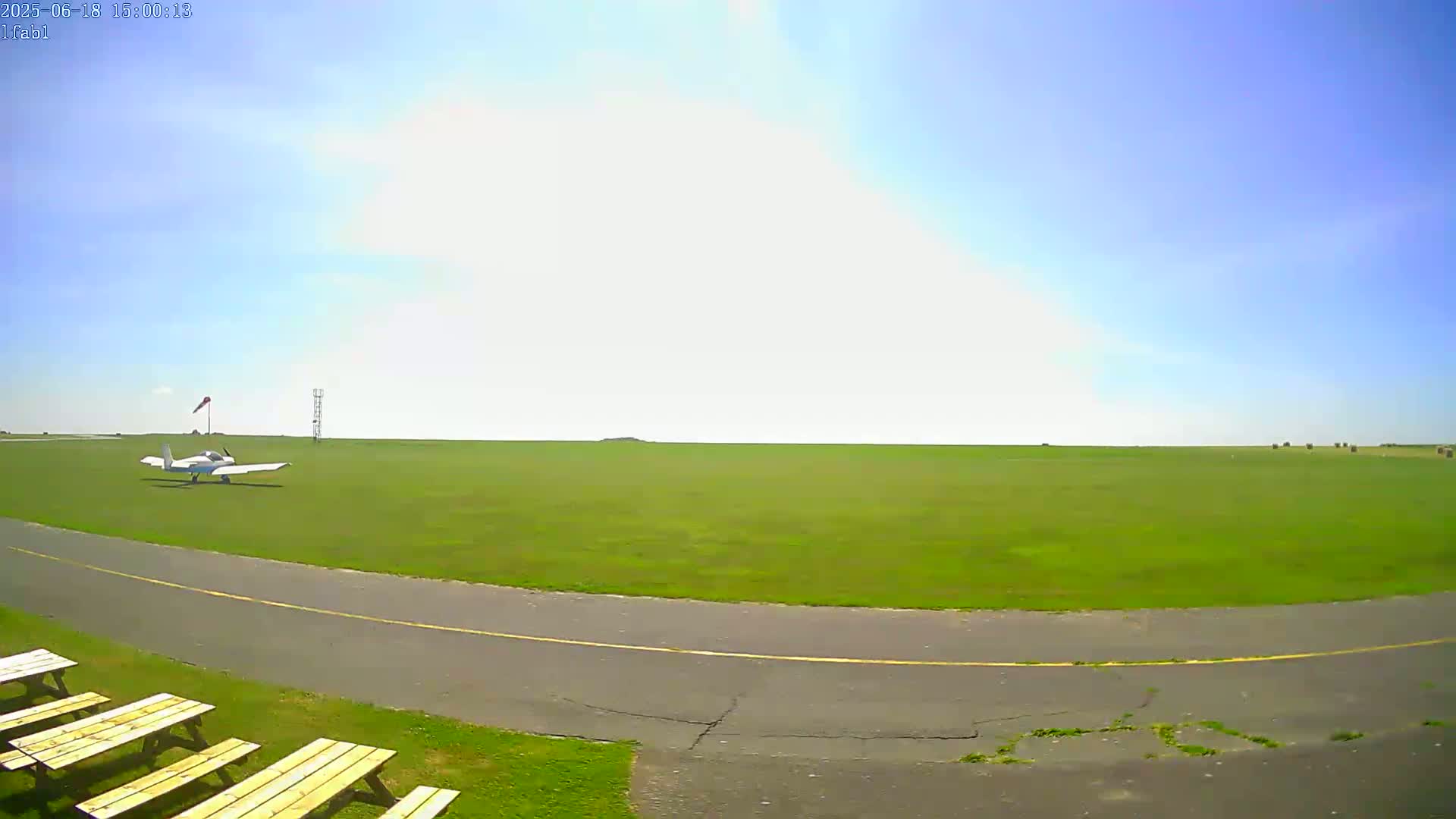A small airplane sits on a grassy airfield under a clear blue sky.