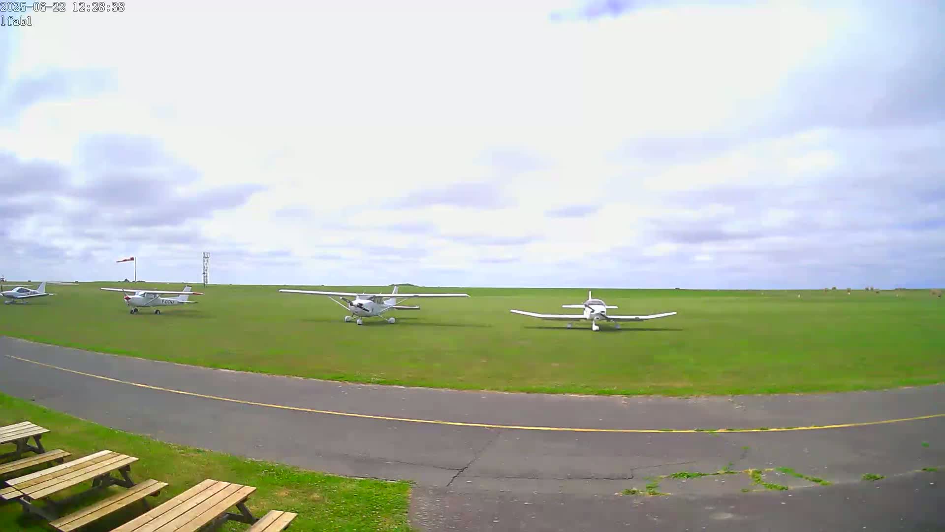 Several small airplanes are parked on a grassy airfield under a mostly cloudy sky.