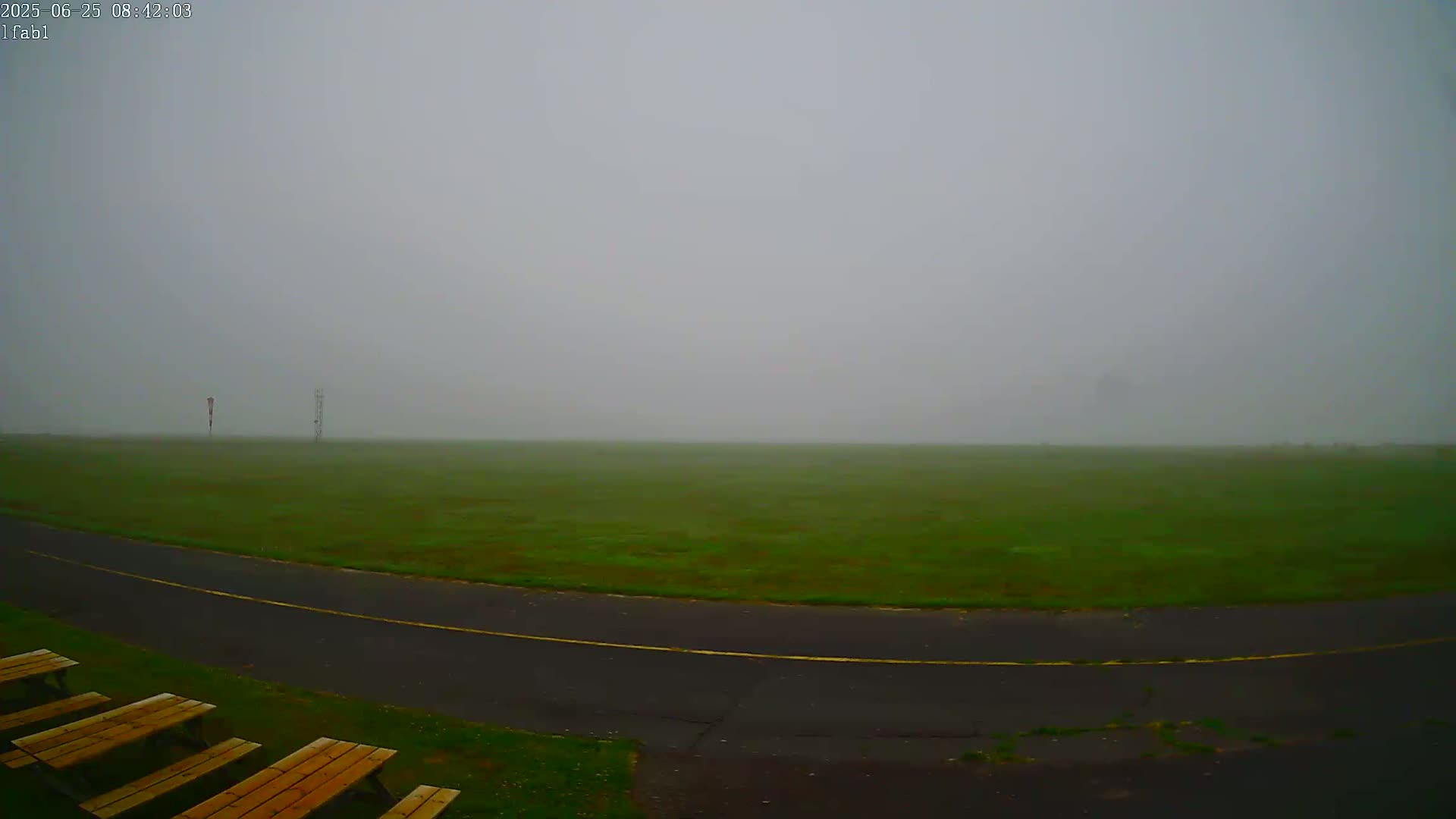 A foggy field is visible beyond a paved road and several wooden picnic tables.