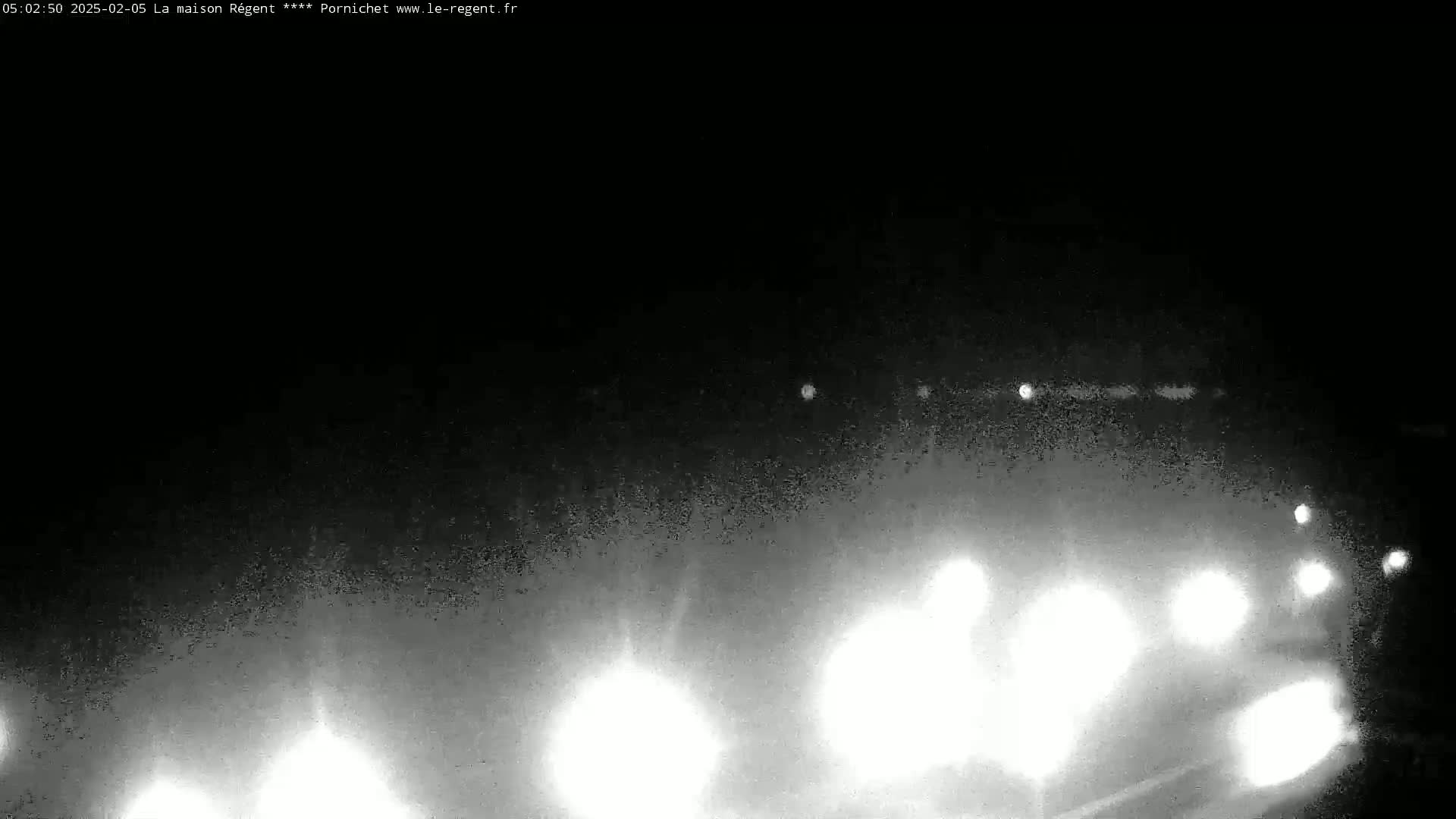 At night, in foggy conditions, the headlights of several vehicles are visible in the distance on a road.