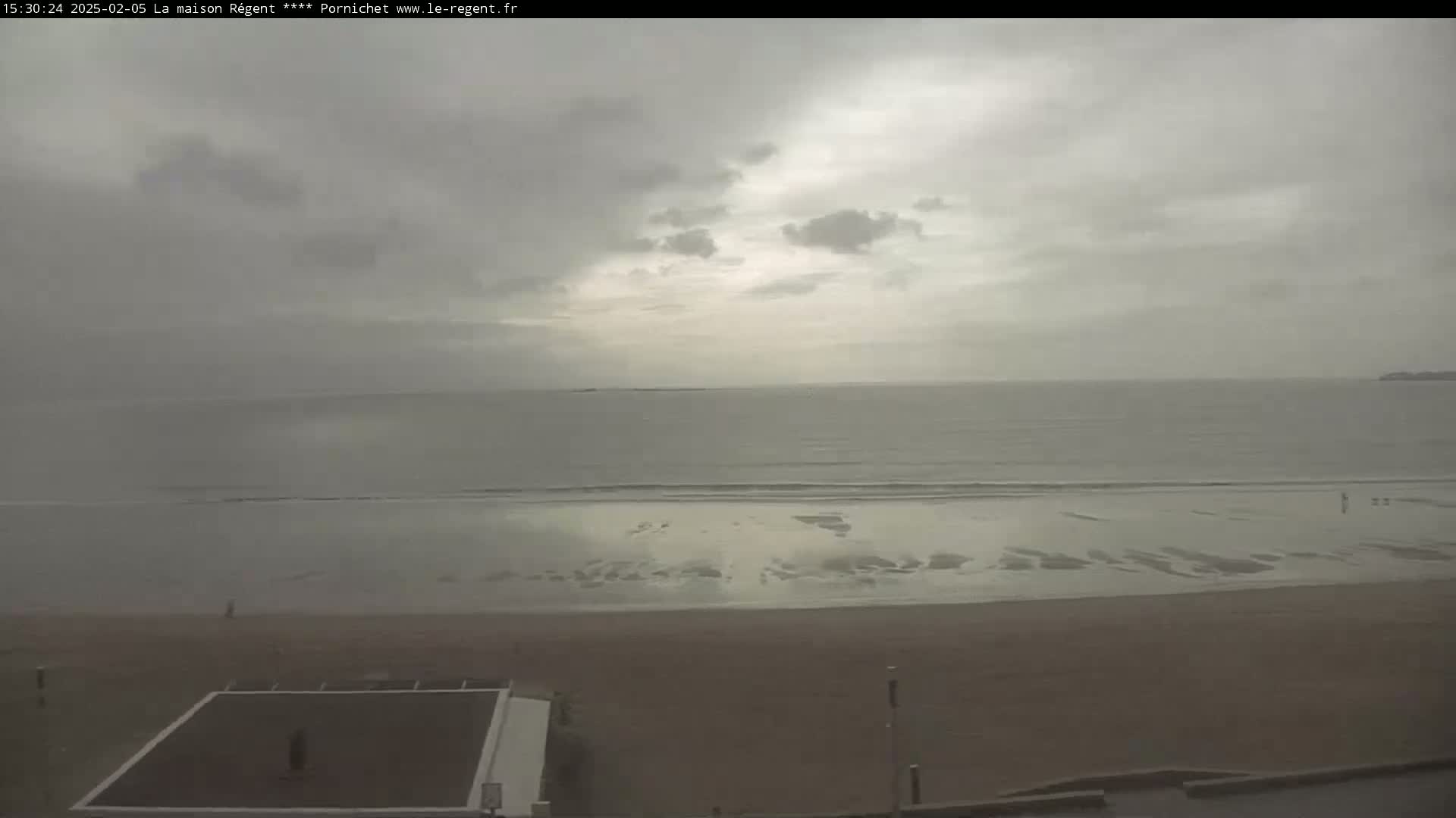 A mostly cloudy sky overlooks a wide, sandy beach and calm ocean.