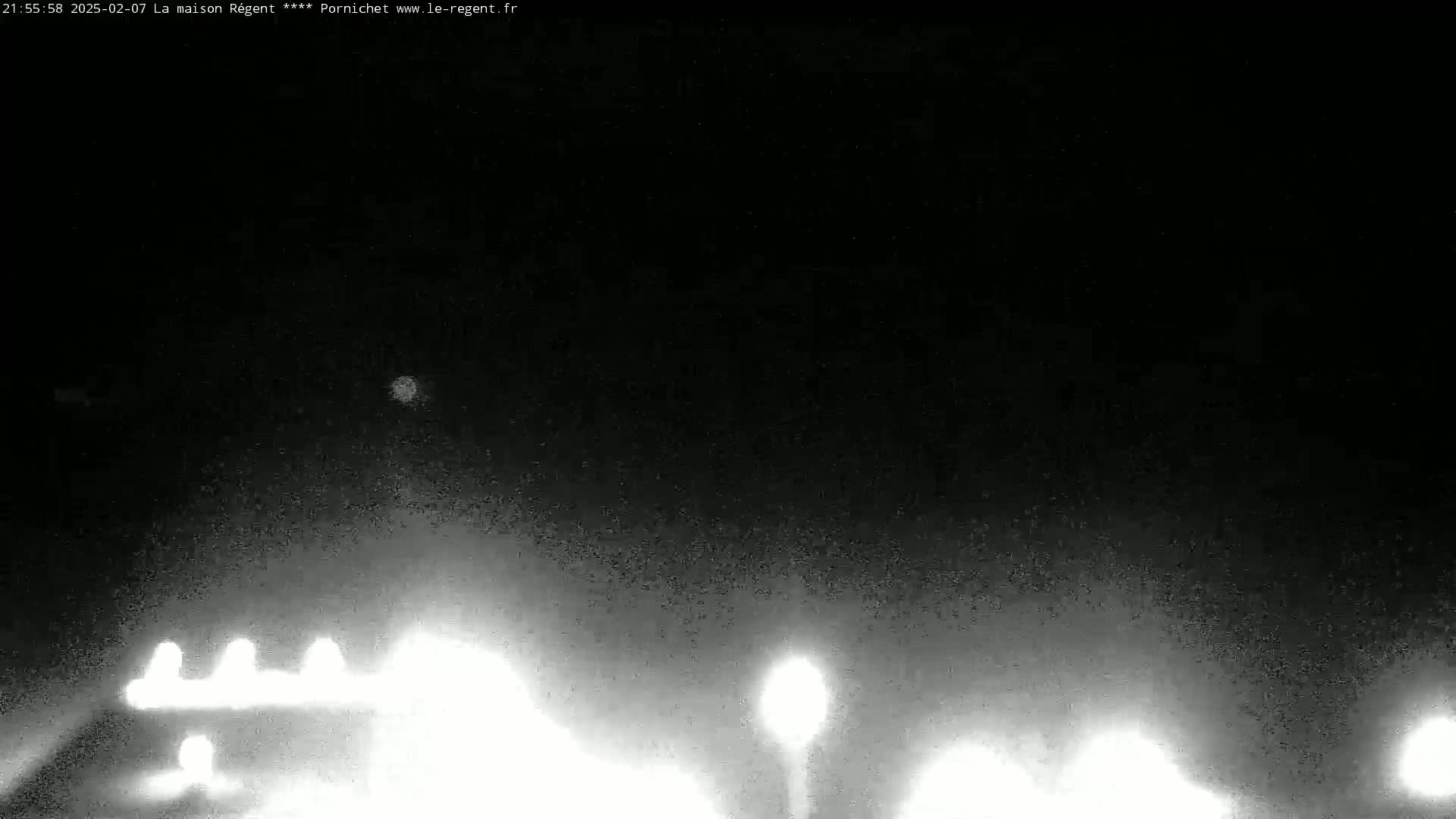 At night, under a dark sky, several sets of vehicle headlights are visible on a road, illuminated by streetlights.