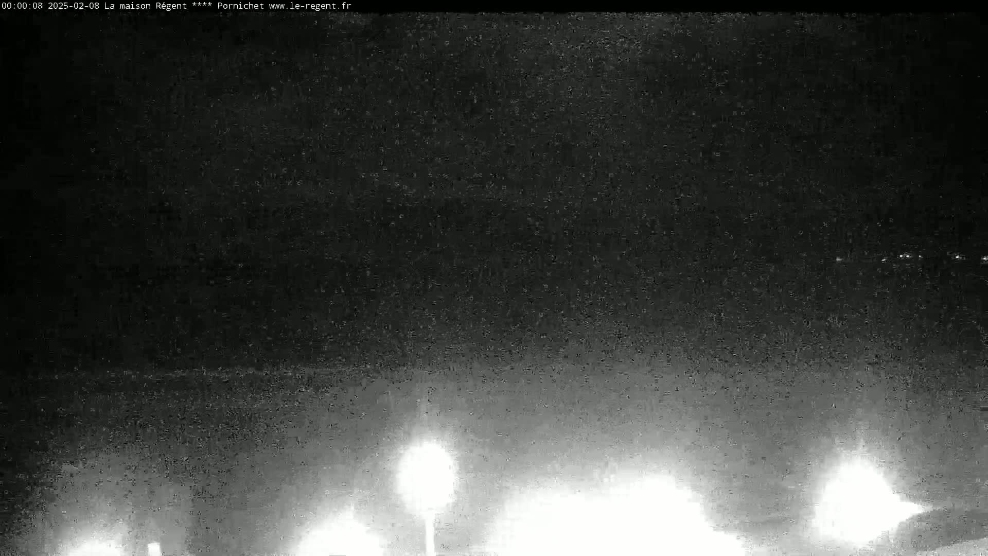 A nighttime, low-light image shows a dark, possibly overcast sky with several distant lights visible on the horizon and a few brighter lights closer to the bottom of the frame.